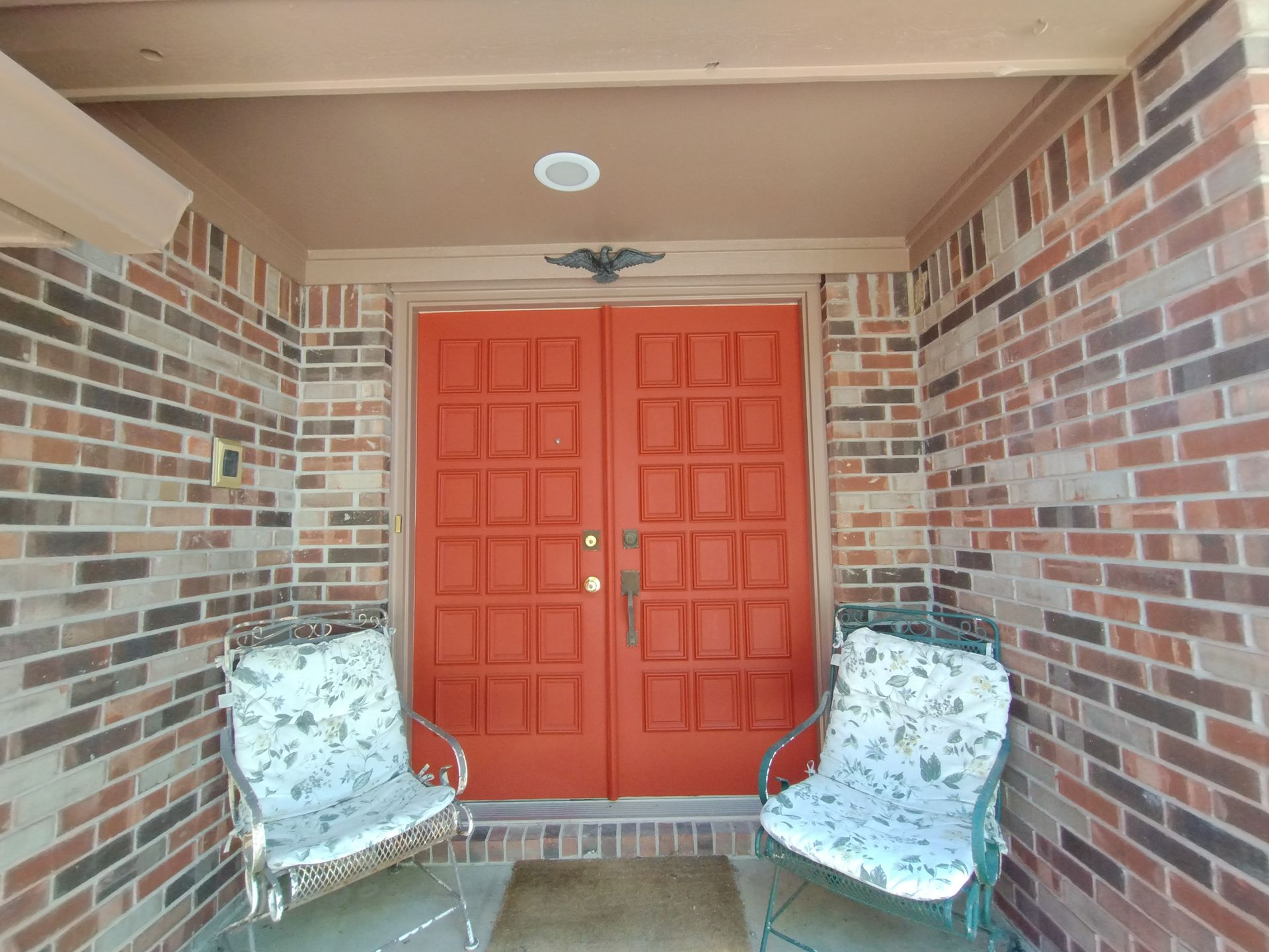 Red double doors on a brick porch with two patterned chairs.