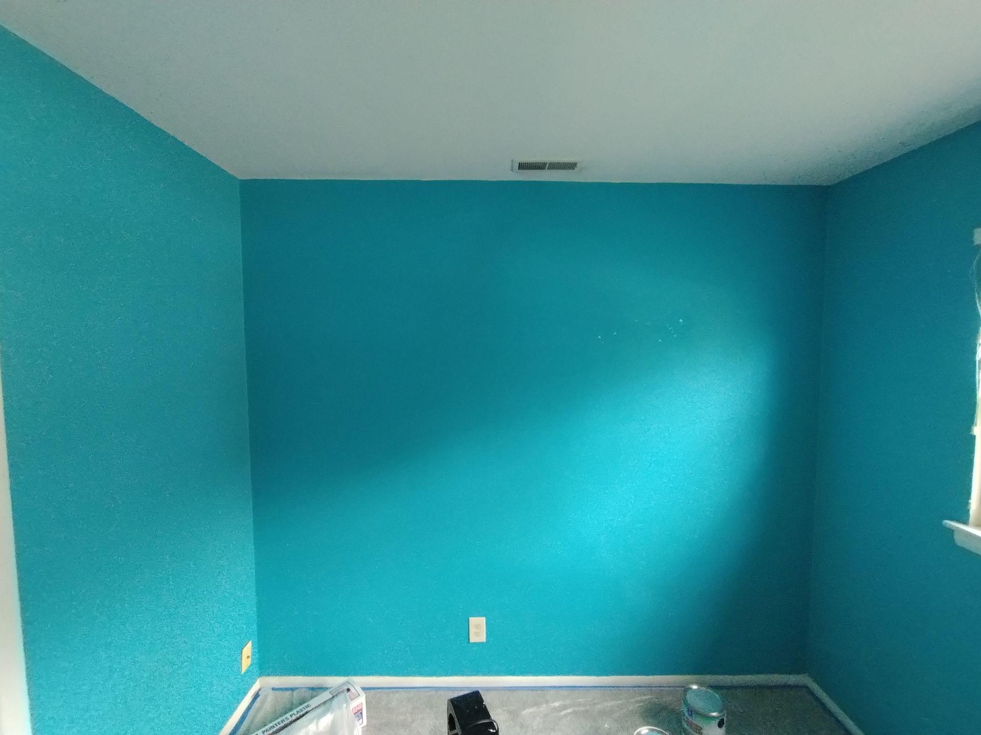 Room with bright blue walls and a white ceiling, empty with some painting supplies on the floor.