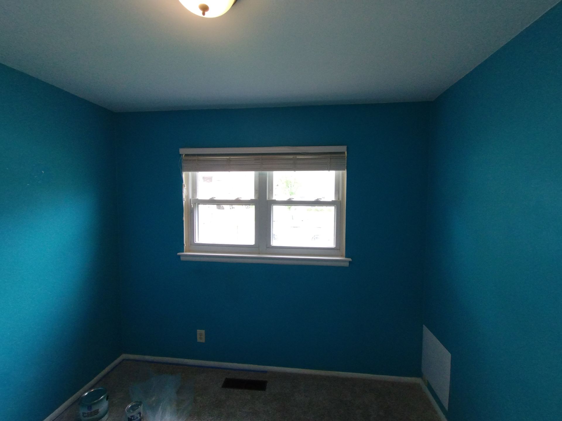 A small room with bright teal walls, white-framed window, and beige carpet.