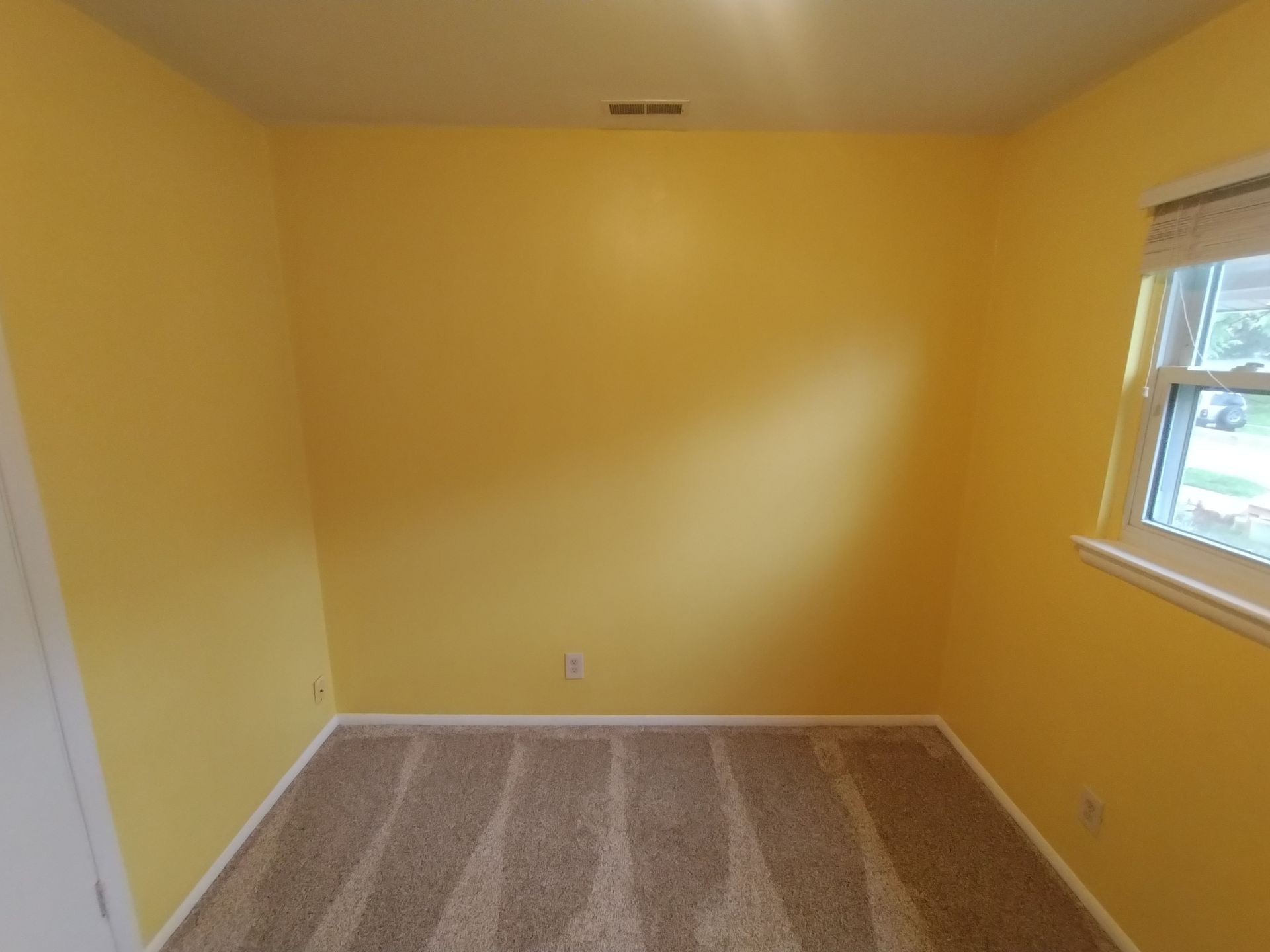 Empty room with yellow walls, tan carpet, and small window.