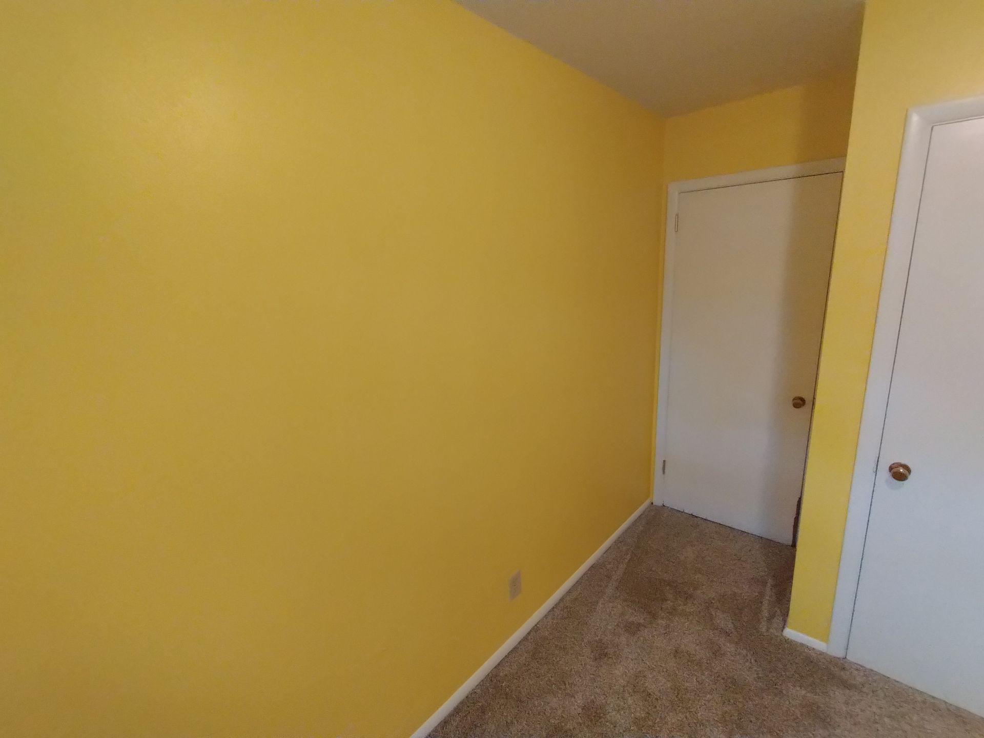 Yellow walls, two white doors in a room with brown carpet.