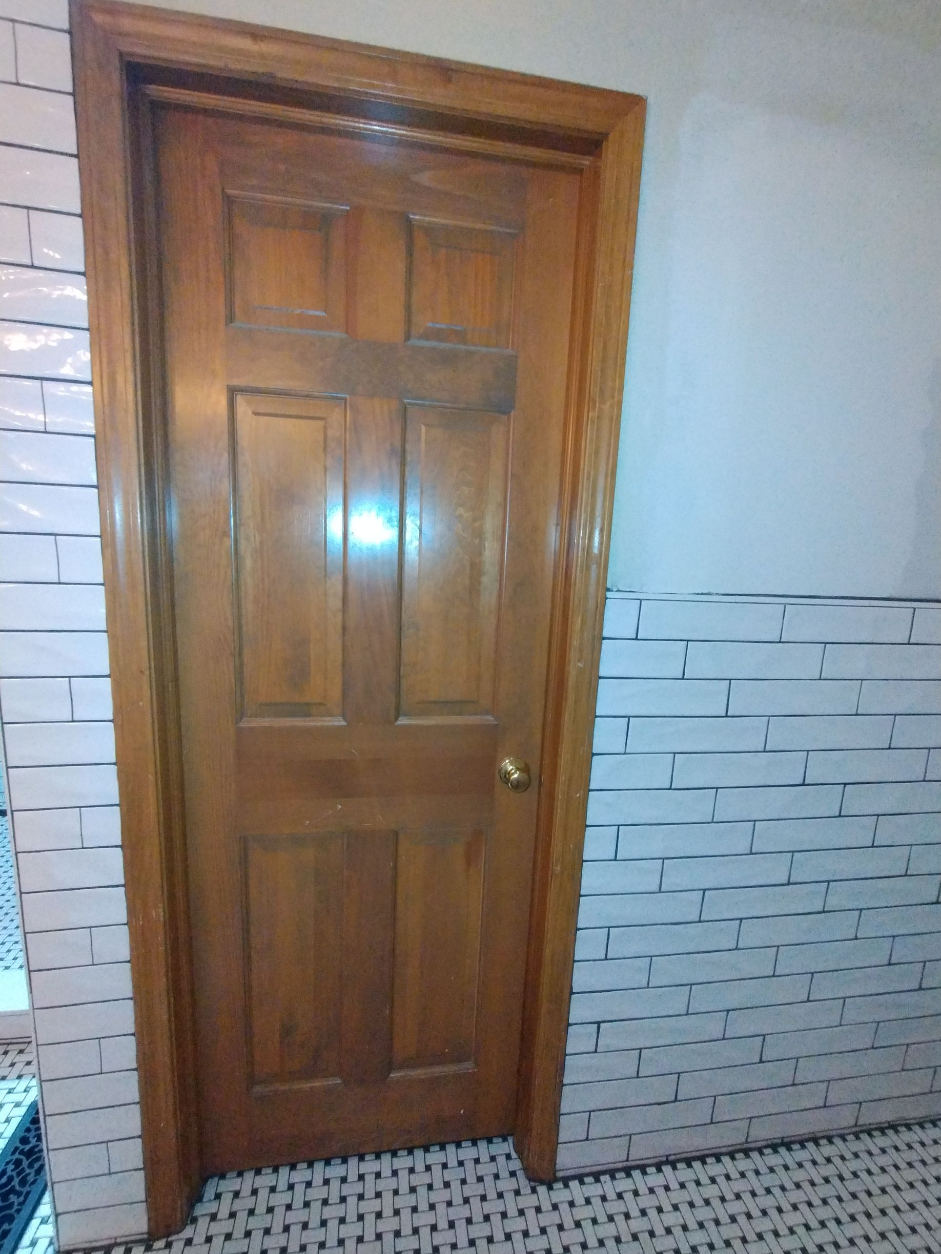 Wooden door with a gold doorknob, set against a white brick wall.