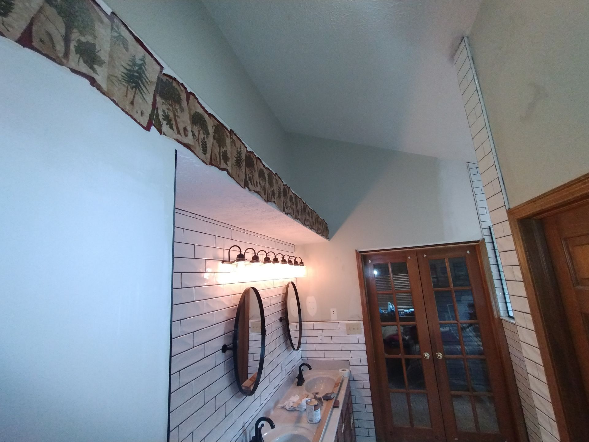 Bathroom with white subway tile, two mirrors, and a wooden door.
