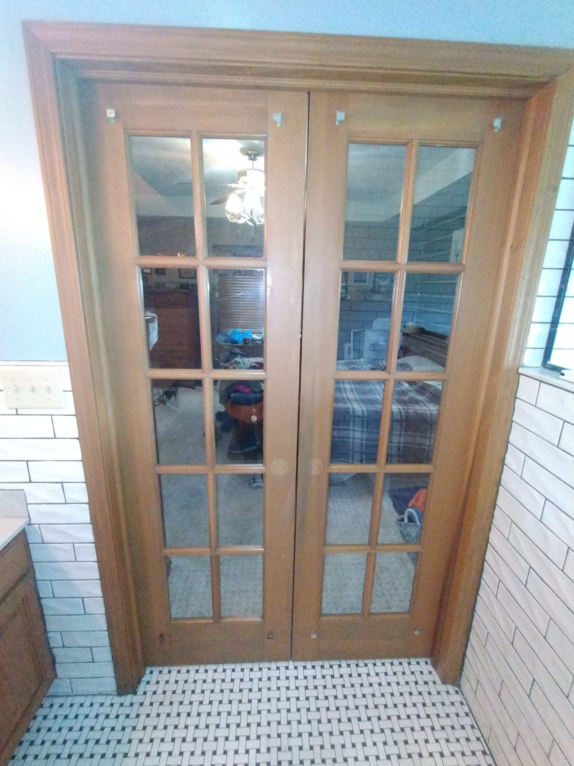 Wooden double doors with glass panes lead into a room with furniture, viewed from a tiled floor.