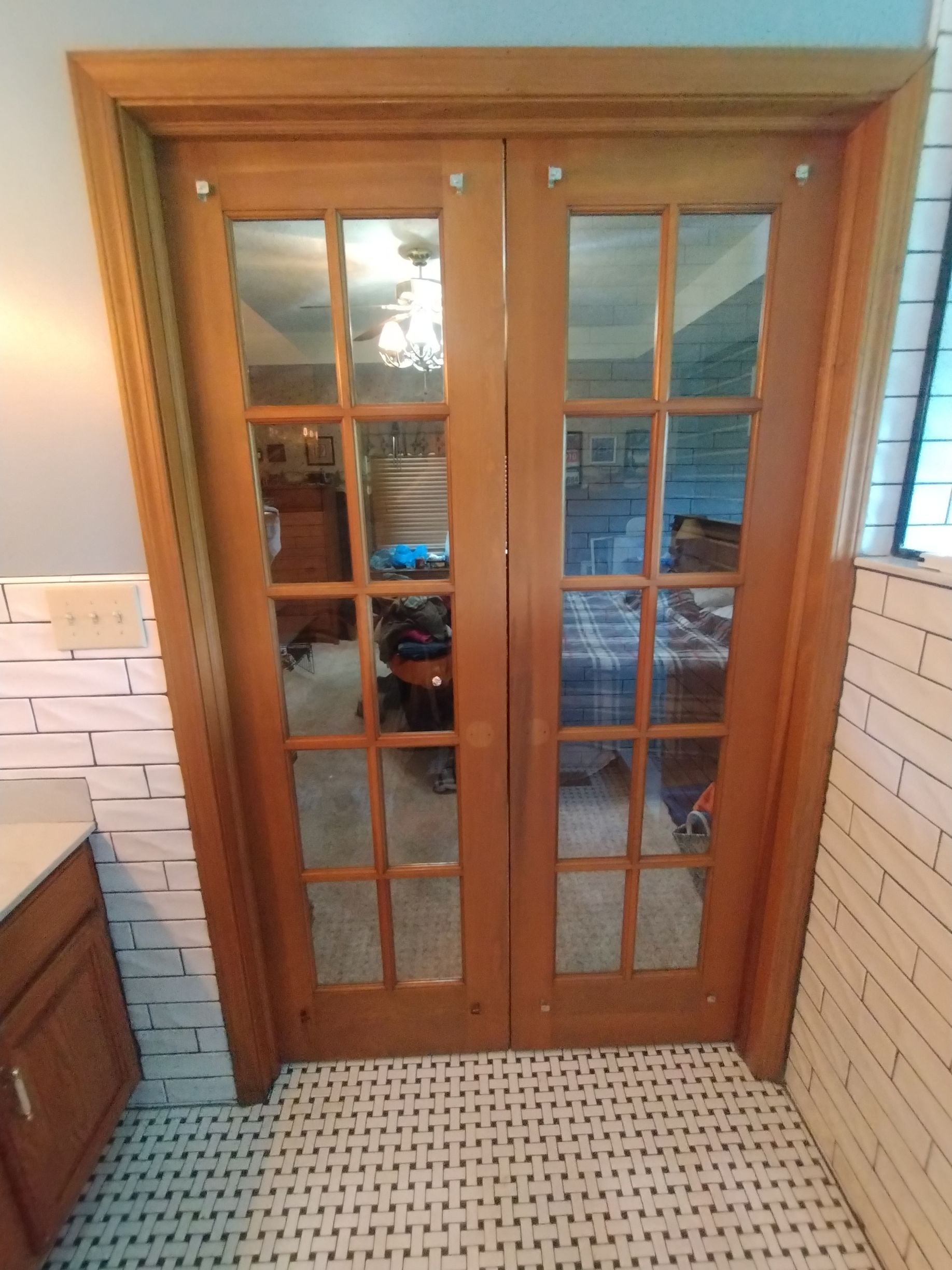 Wooden French doors with glass panes in a bathroom with tile floor and white brick-like walls.