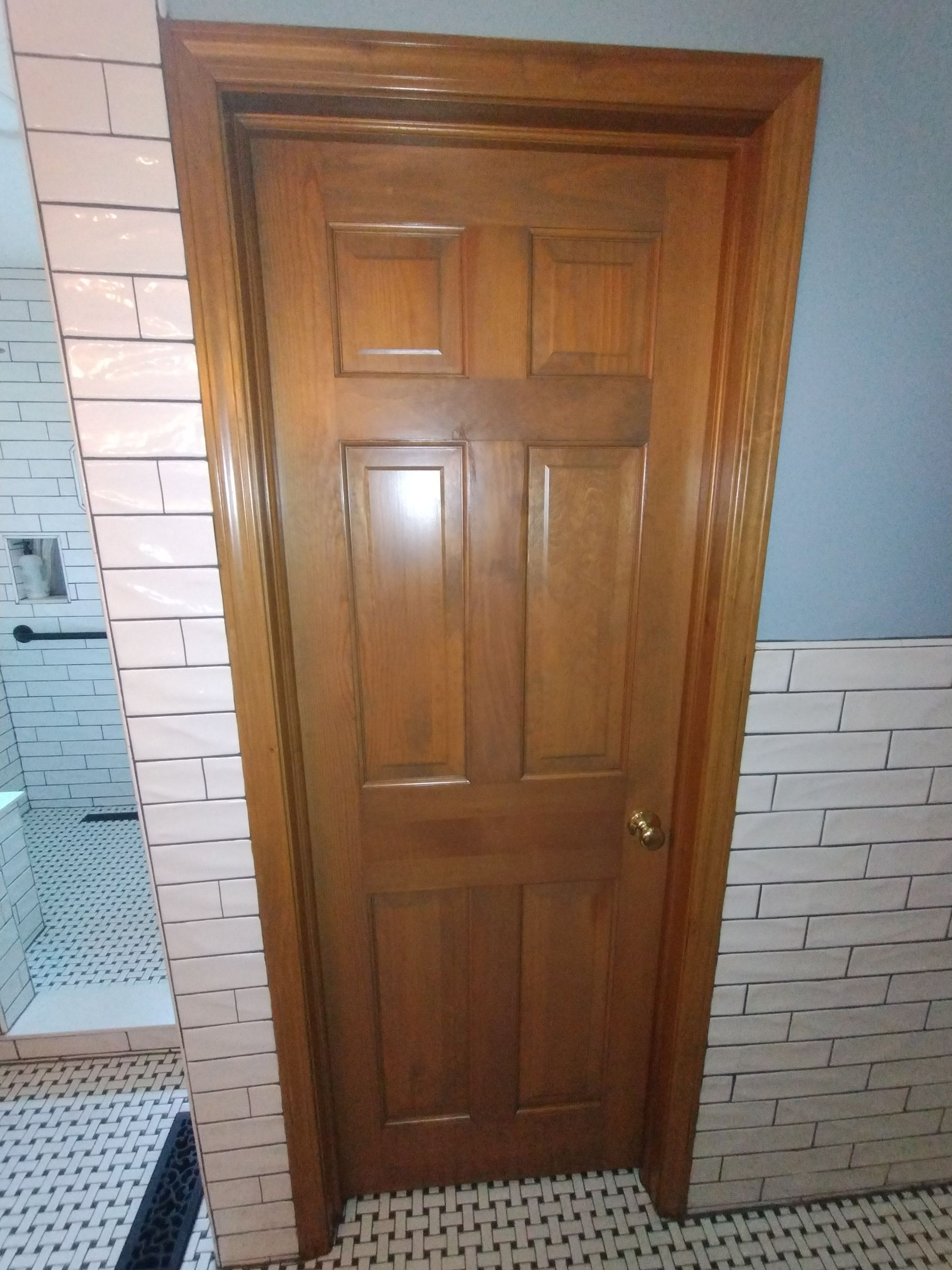 Wooden door in a bathroom with white brick-style tile and black and white floor tiles.