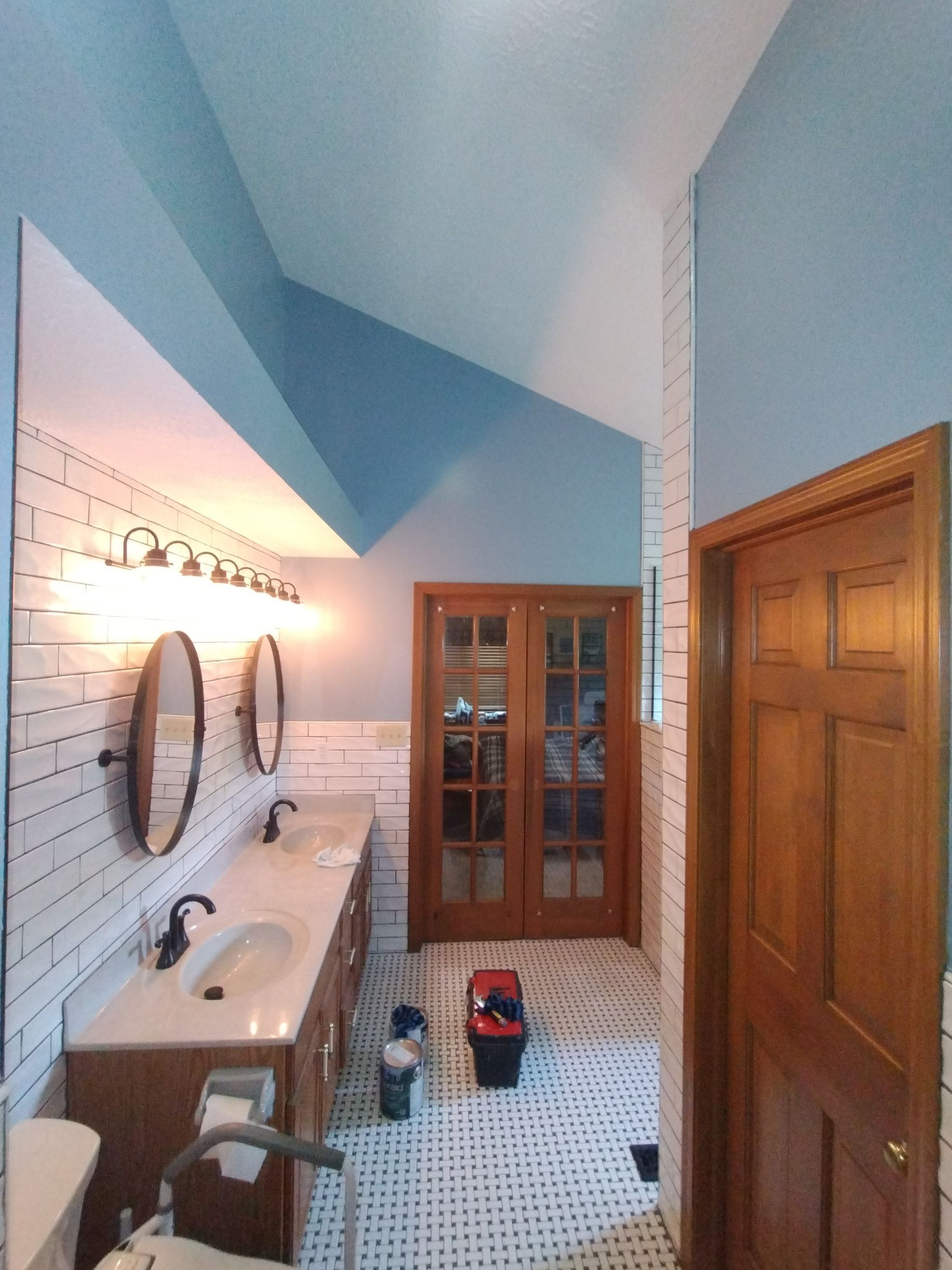 Bathroom with double vanity, oval mirrors, and blue walls. Doorways lead to other rooms.