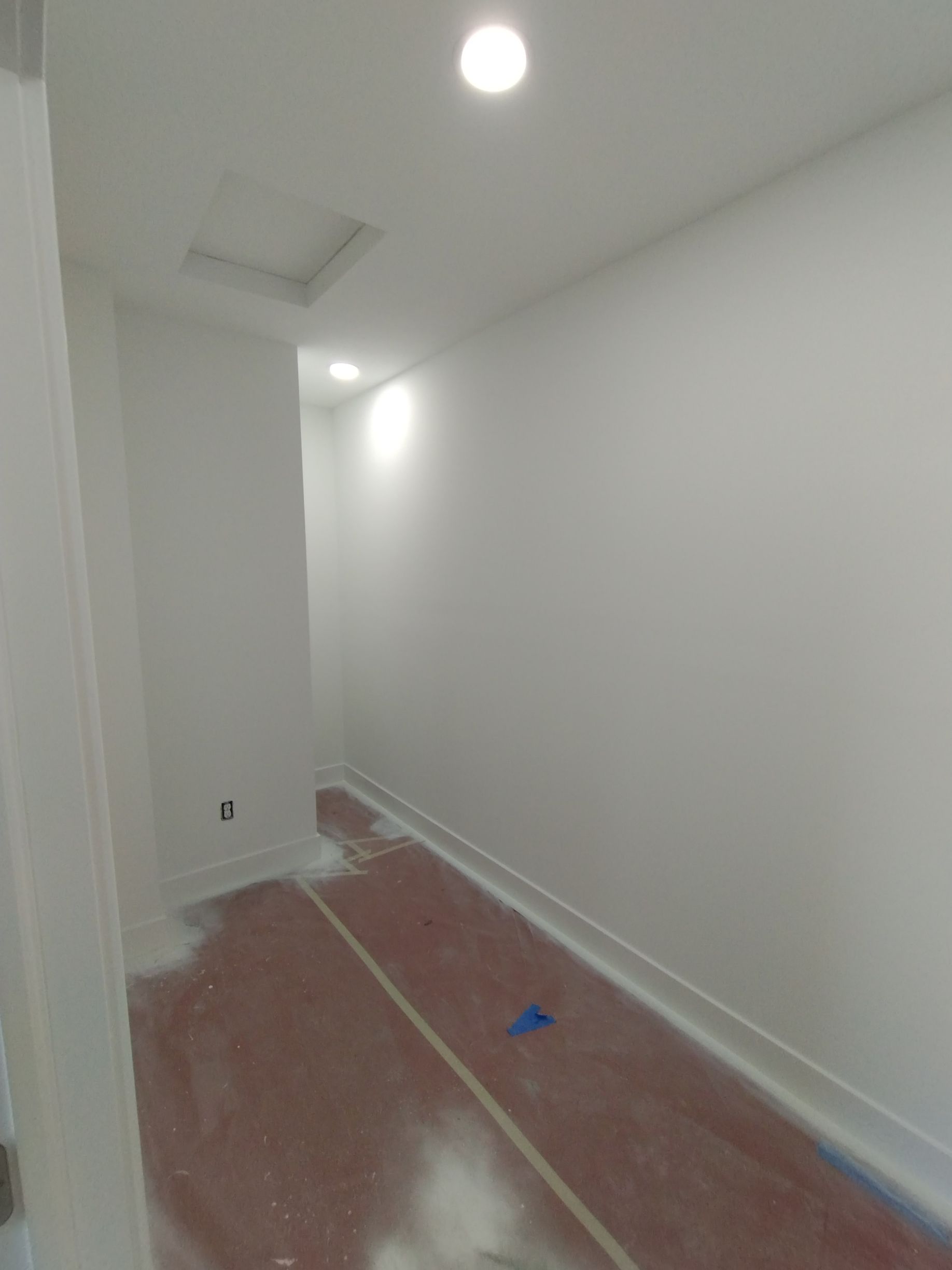Small, white-painted room with a red floor. Ceiling lights shine, and the baseboards are white.