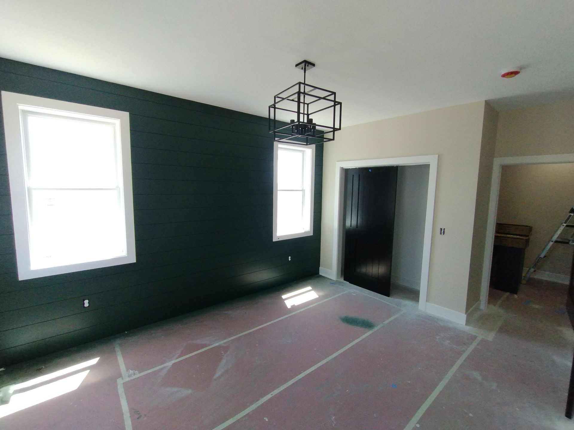 Room with dark green wall, two white-framed windows, square light fixture, and open doorway. Pink floor covering.