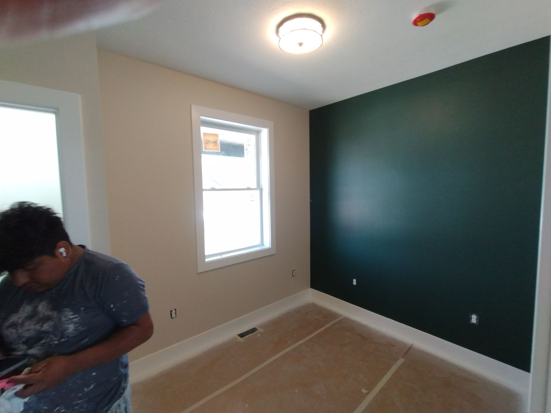 Room with green accent wall, window, beige walls, worker in blue shirt.