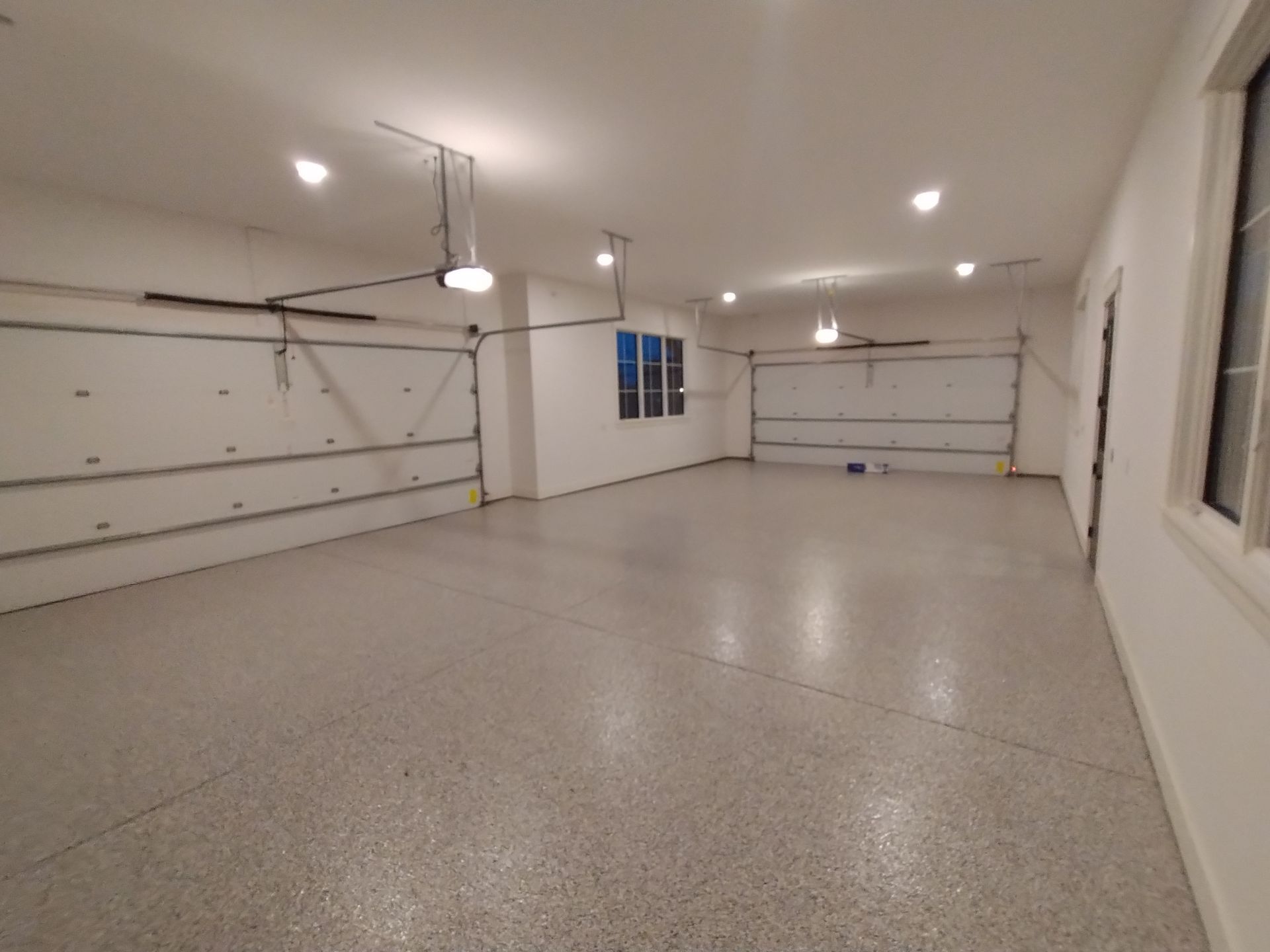 Empty, spacious garage with epoxy floor, white walls, and two garage doors.