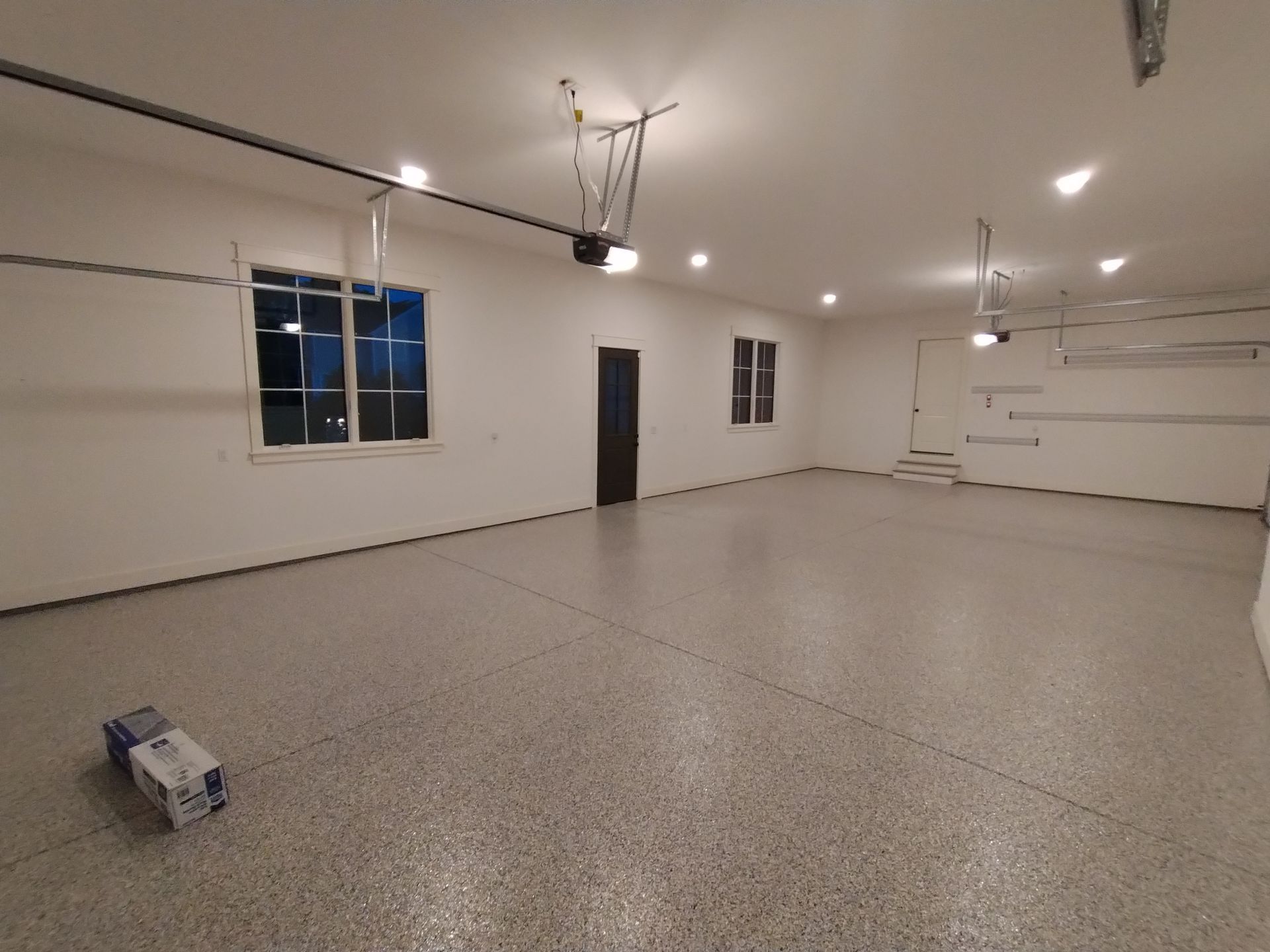 Empty garage with epoxy floor, windows, and closed door.
