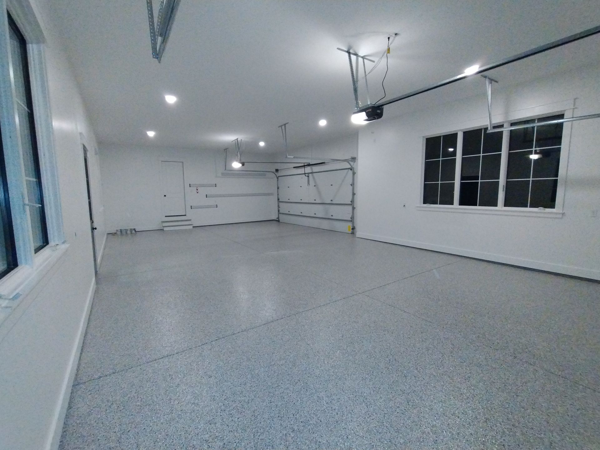 Empty, newly painted garage with epoxy floor, two windows, and garage door track.