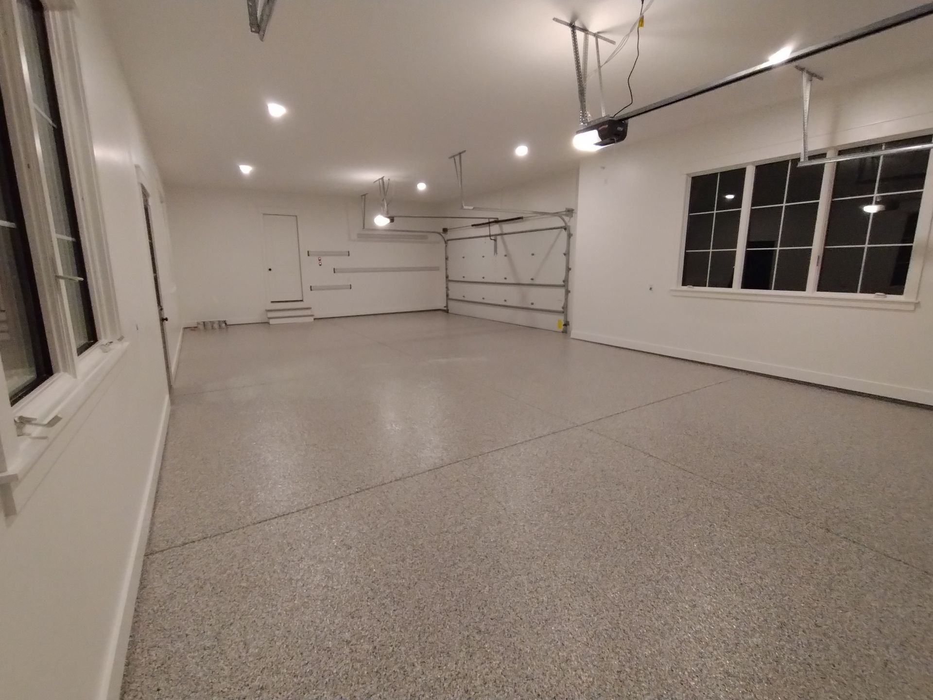 Empty, newly painted garage with speckled gray floor and white walls. Door and windows are visible.