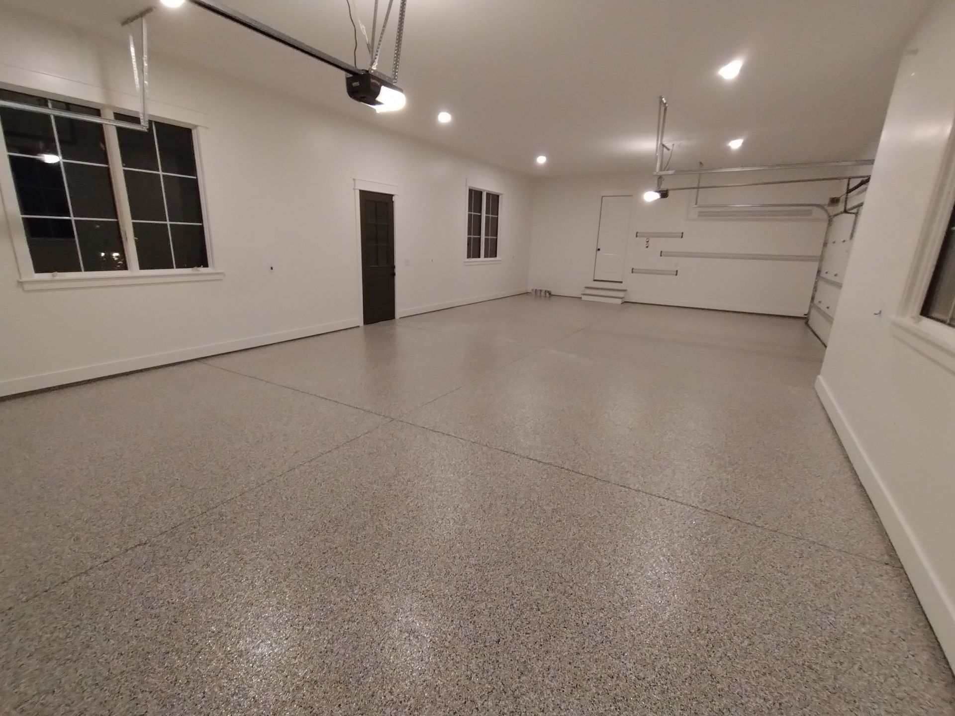 Empty, clean garage with epoxy flooring. White walls, two windows, closed garage door, overhead lights.