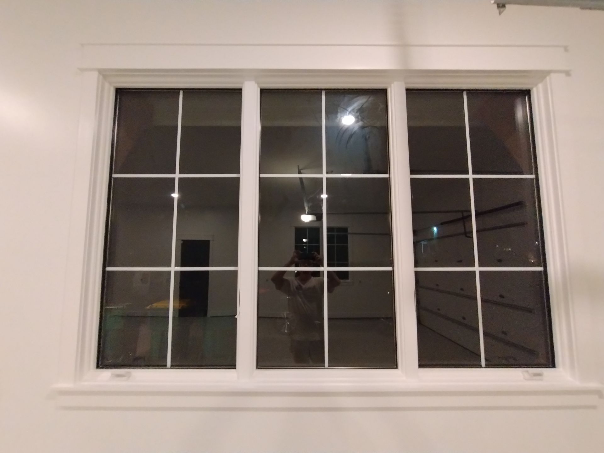 White-framed window with grid panes reflecting interior of a room, showing a person, dark door, and garage door.