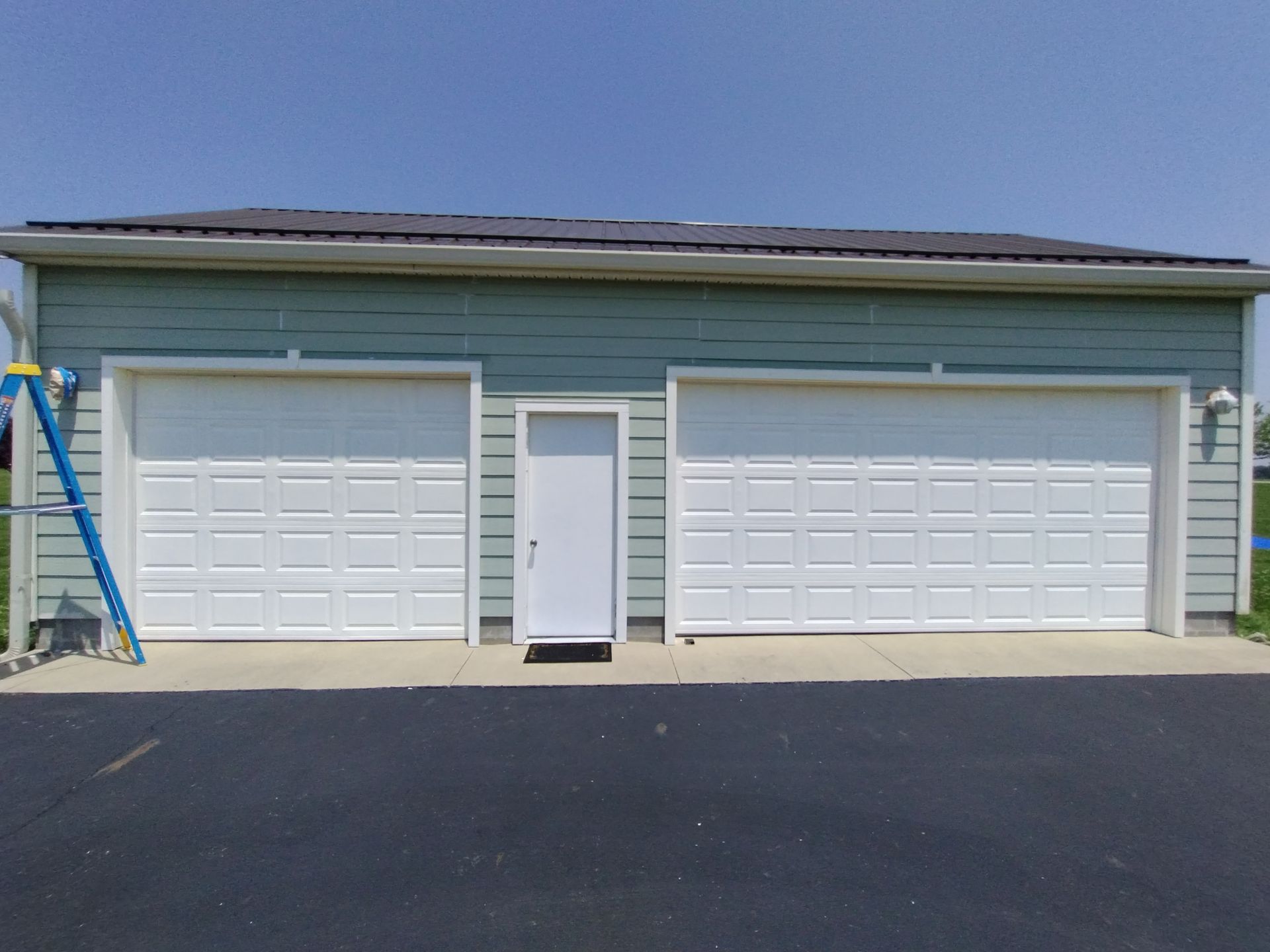 A two-car garage with a white door, a small door, and teal siding, under a blue sky.