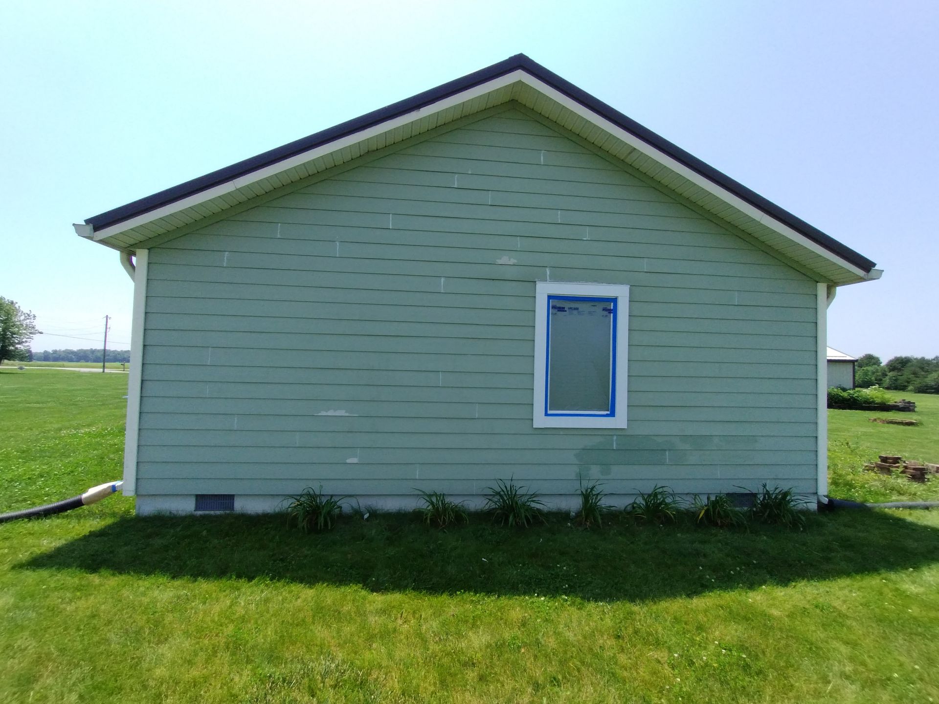 Green-sided building with a window, black roof, and grass in the foreground on a sunny day.