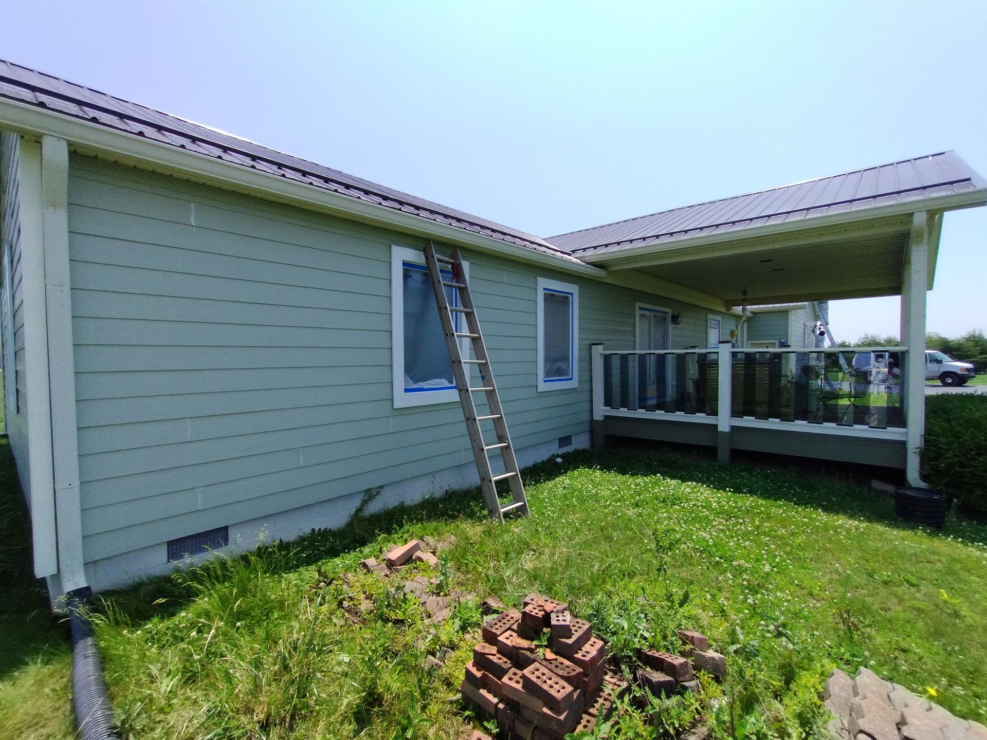 Green house with a metal roof, a ladder leaning against the side, and a small porch area.