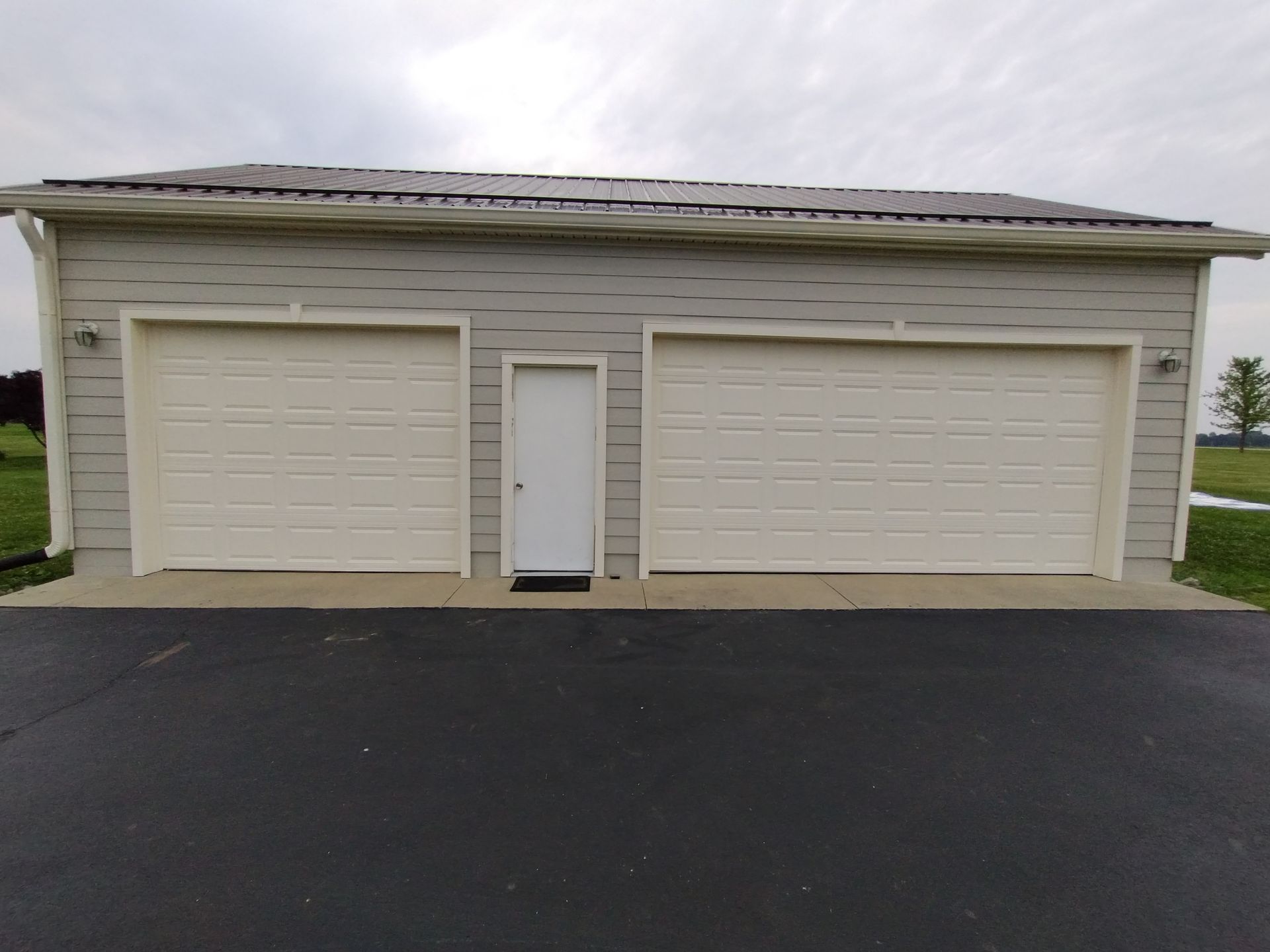 Two-car garage with a small white door between two garage doors on a gray building.