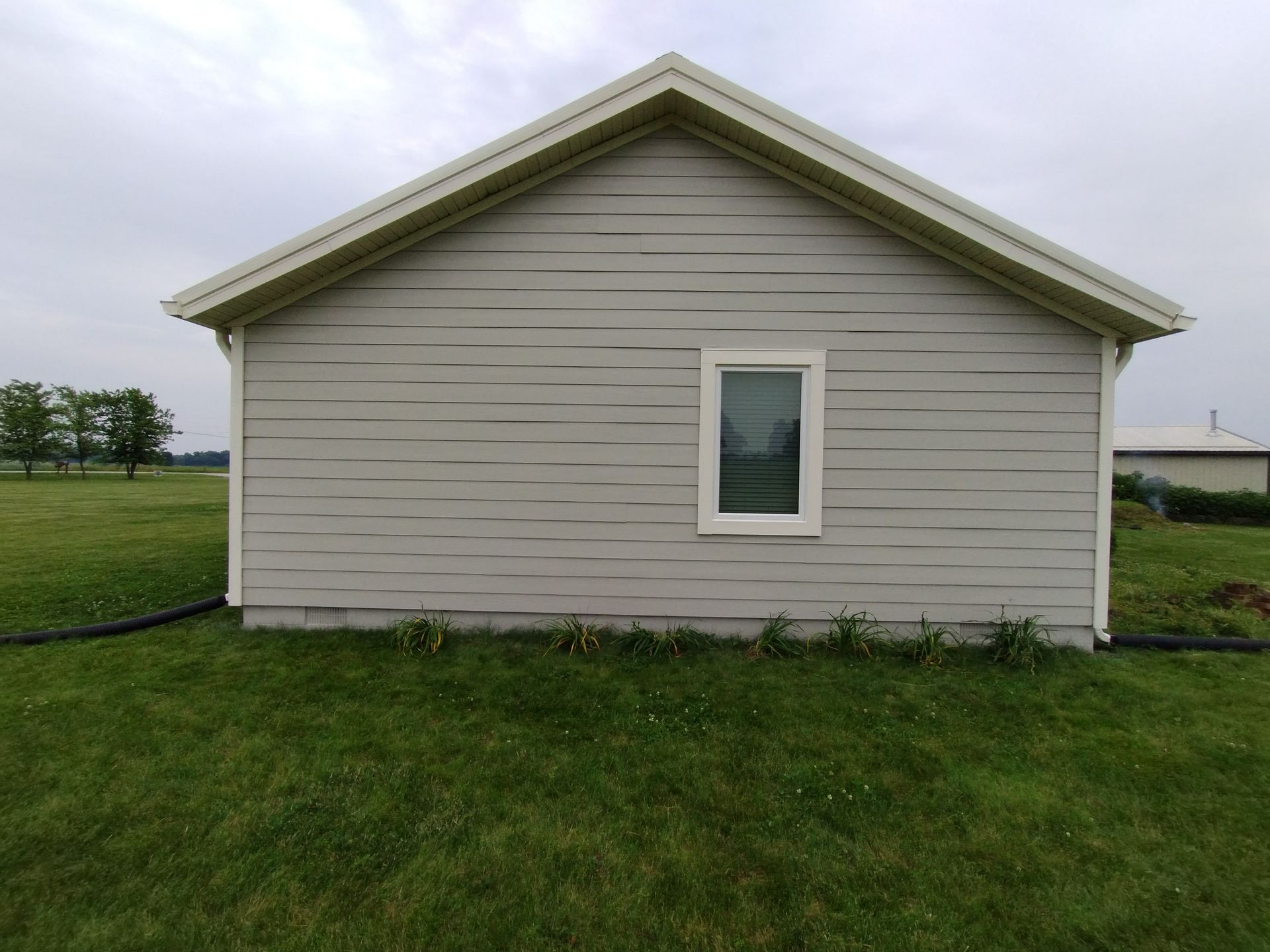 Gray-sided shed with white trim, window, and roof; set on a grassy field under a cloudy sky.