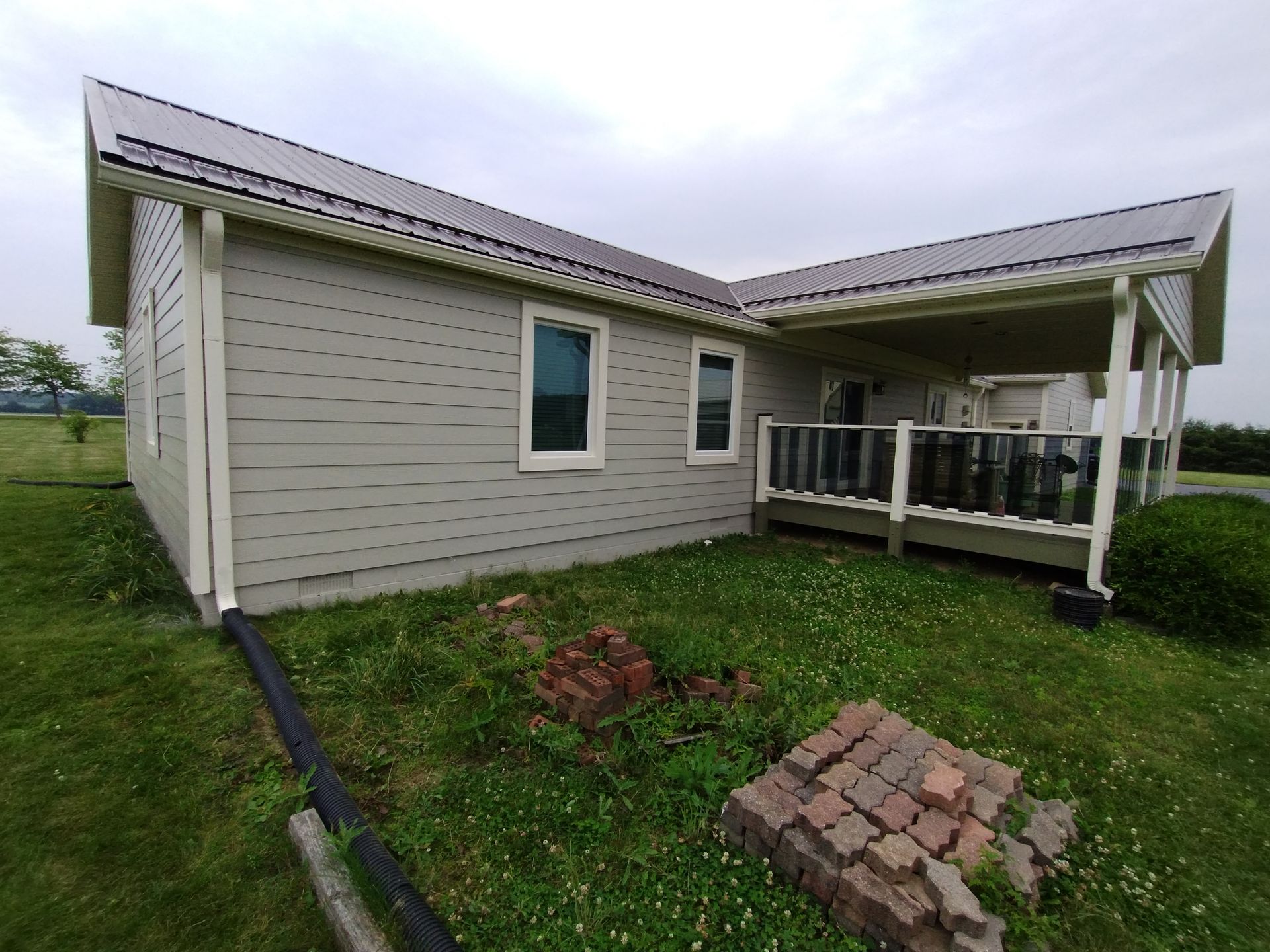 A beige house with a covered porch, gray roof, and white-trimmed windows, surrounded by green grass and cloudy sky.