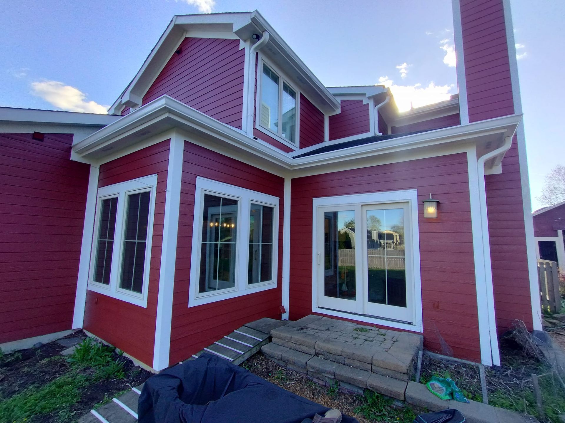 Red house exterior with white trim, windows, and doors, with a brick step and green plants below.