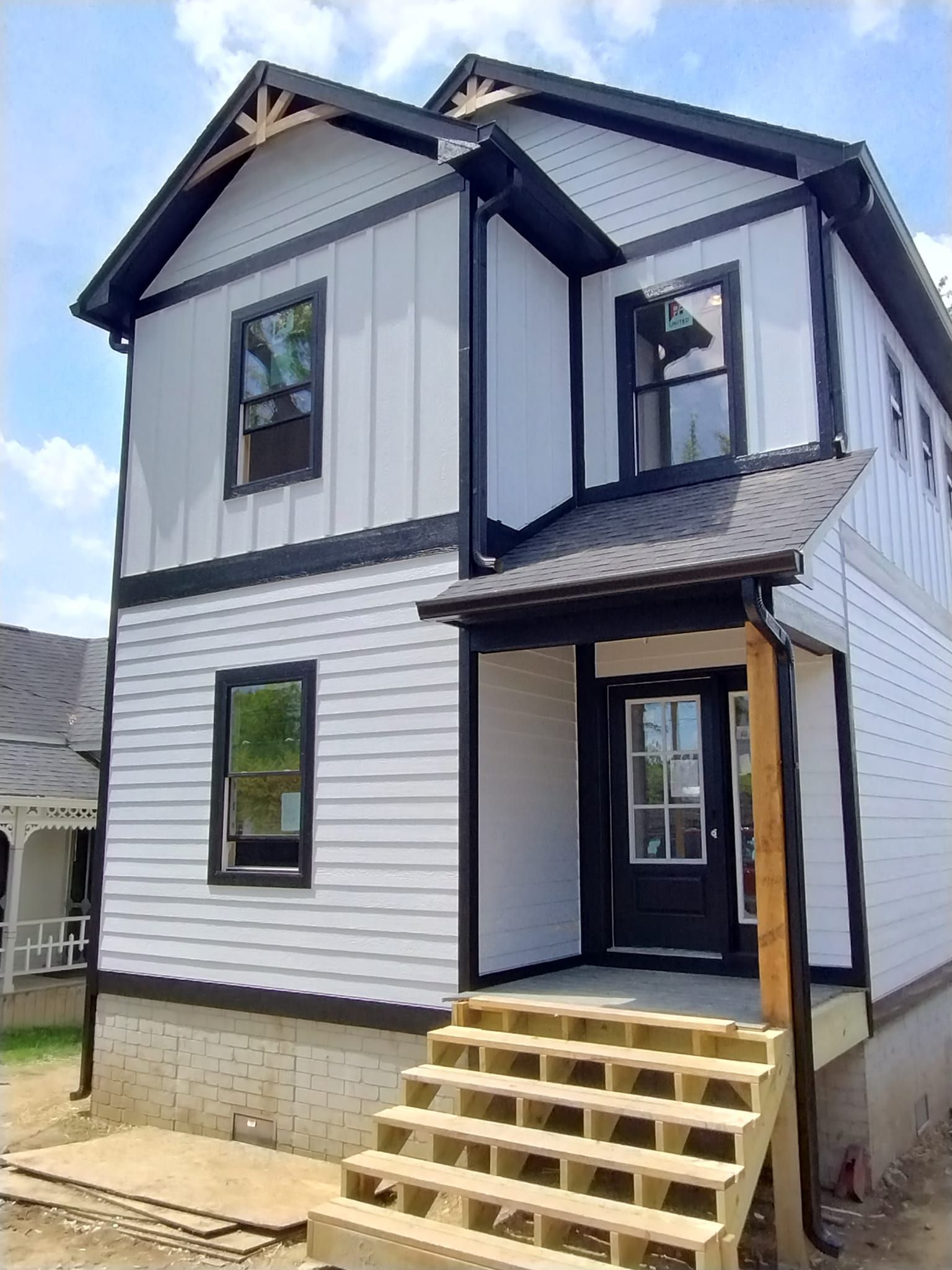Two-story house with white siding and black trim, small front porch, wooden steps, and a black front door.