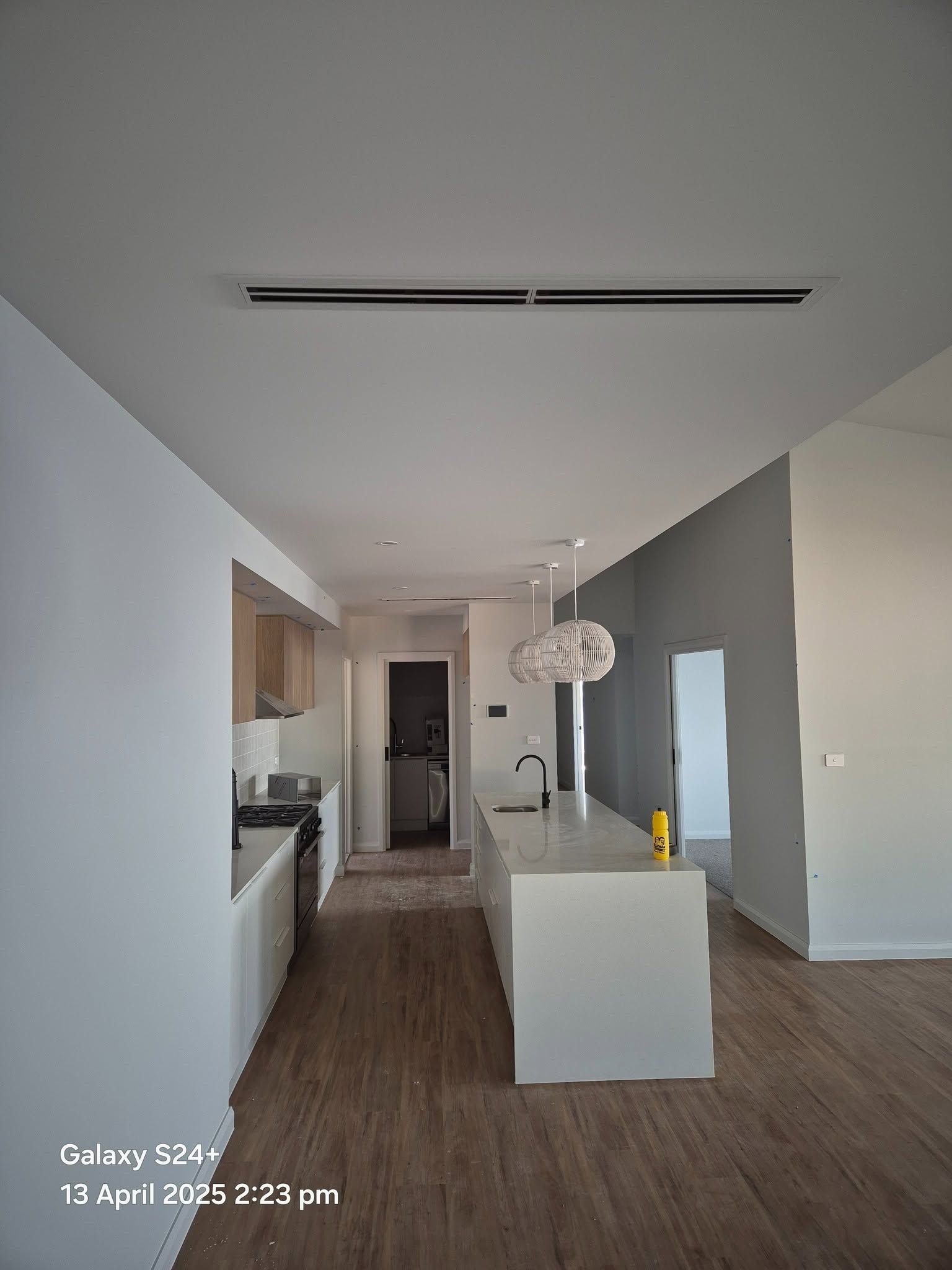 Modern open-plan kitchen and living space with wood floors, white island, gray accent wall, and pendant light