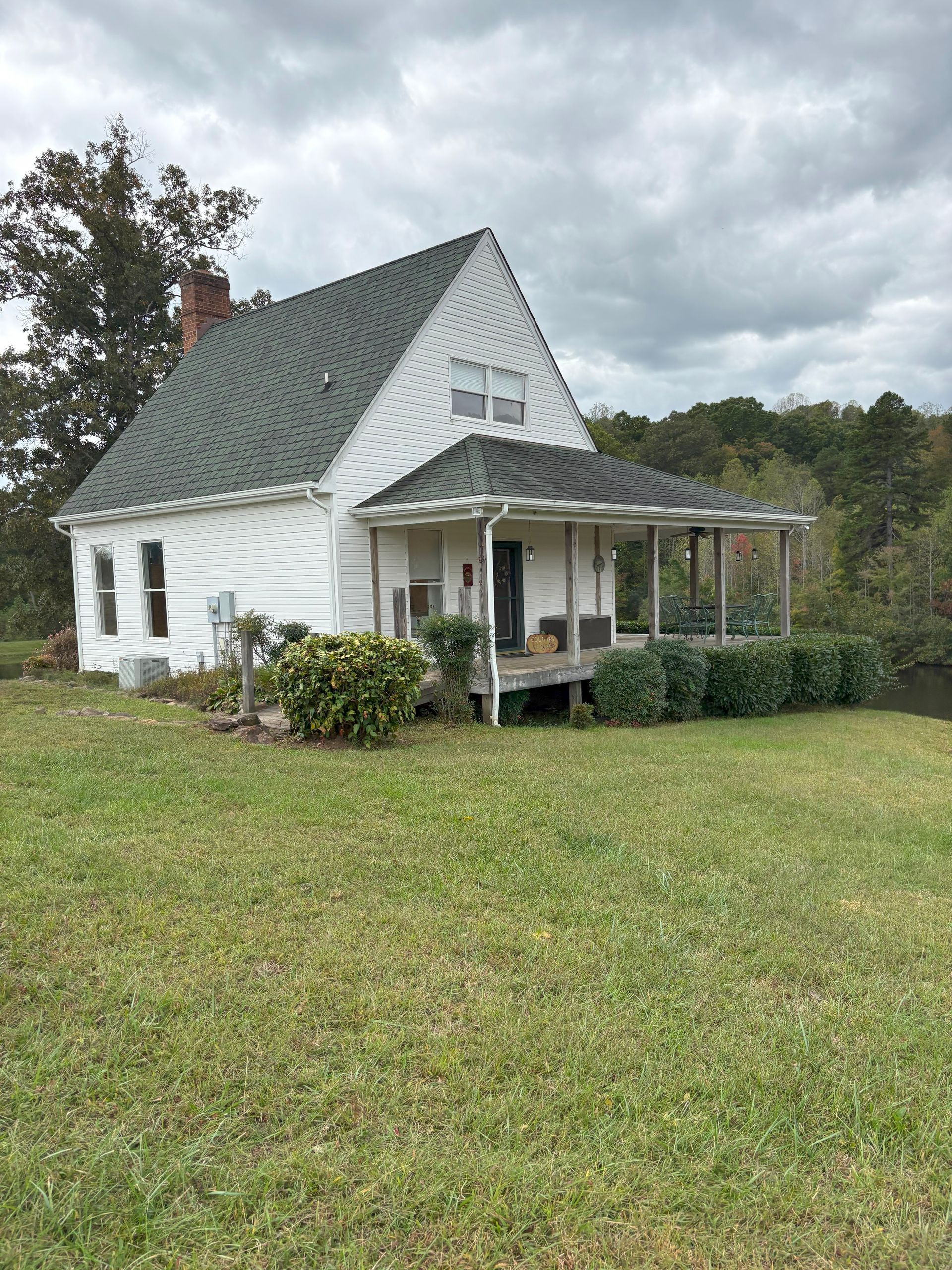 White house with green roof and porch, set on a grassy lawn, under a cloudy sky.