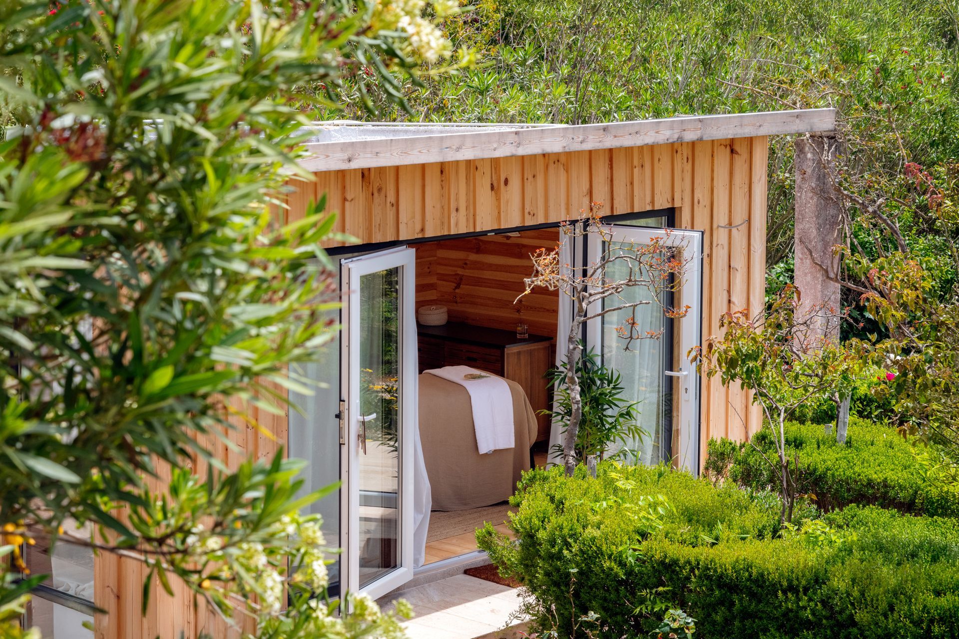 A small wooden house with a bed inside of it surrounded by trees.