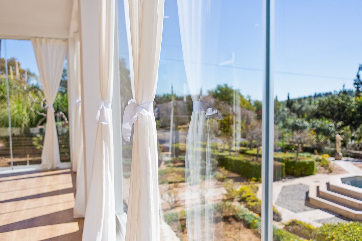A view of a garden through a glass window with white curtains.