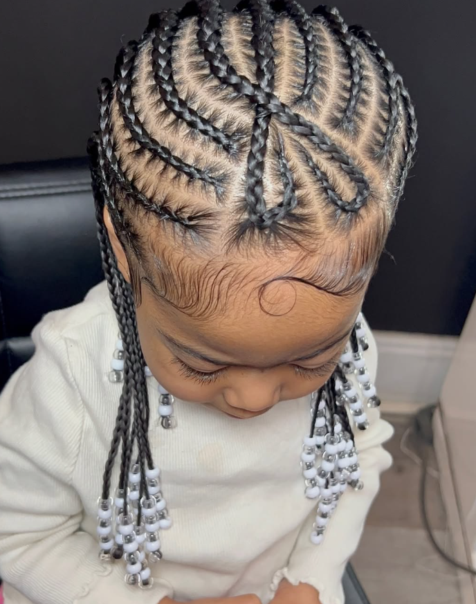 A close-up of hair styled in cornrows featuring a curved, decorative design on the scalp, finished with white beads.