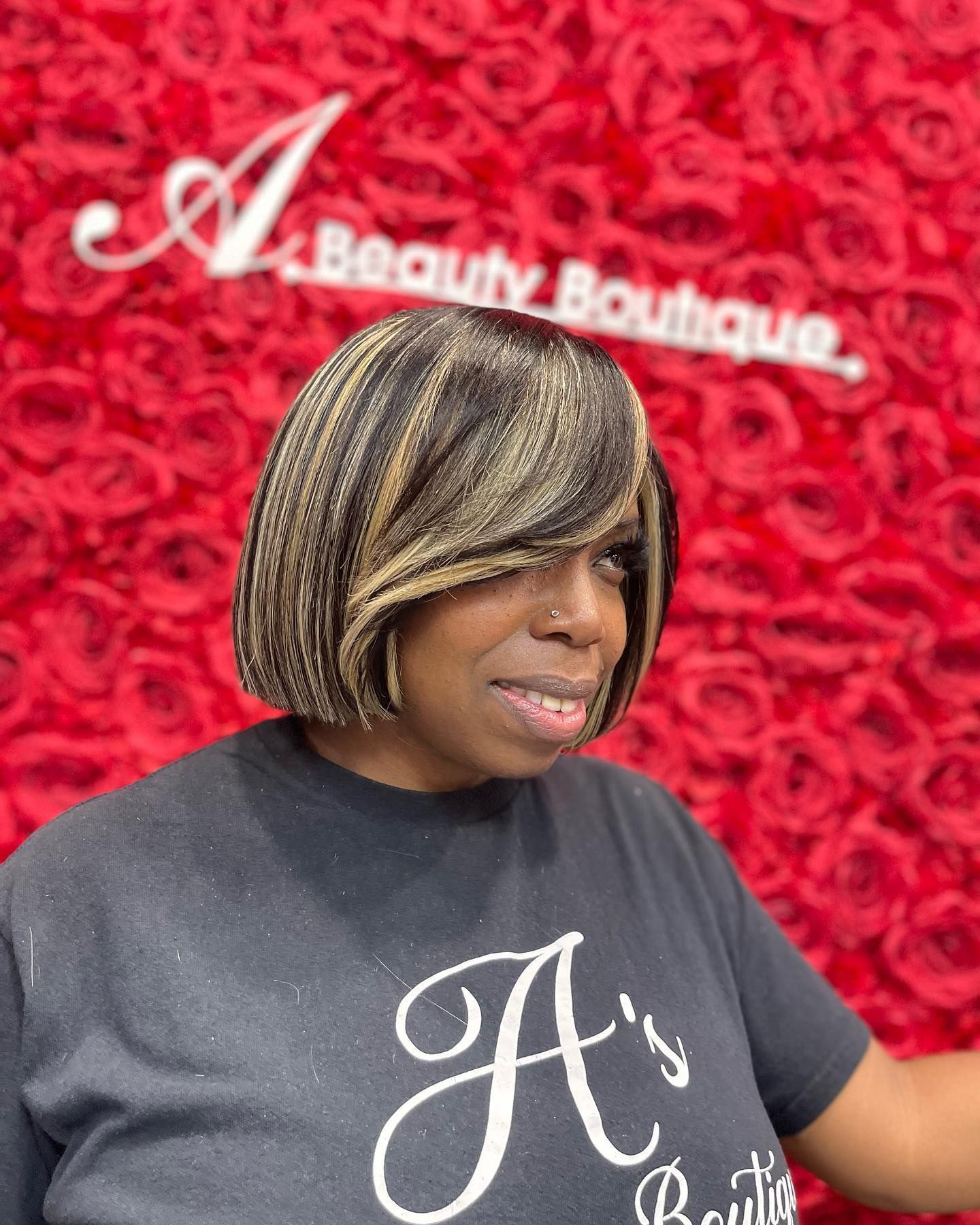 A person with a highlighted bob hairstyle poses in front of a red rose floral wall displaying the