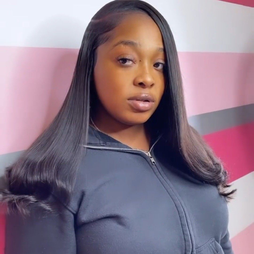 A person with straight, dark hair and a neutral expression, posing in front of a wall with pink, white, and gray stripes.