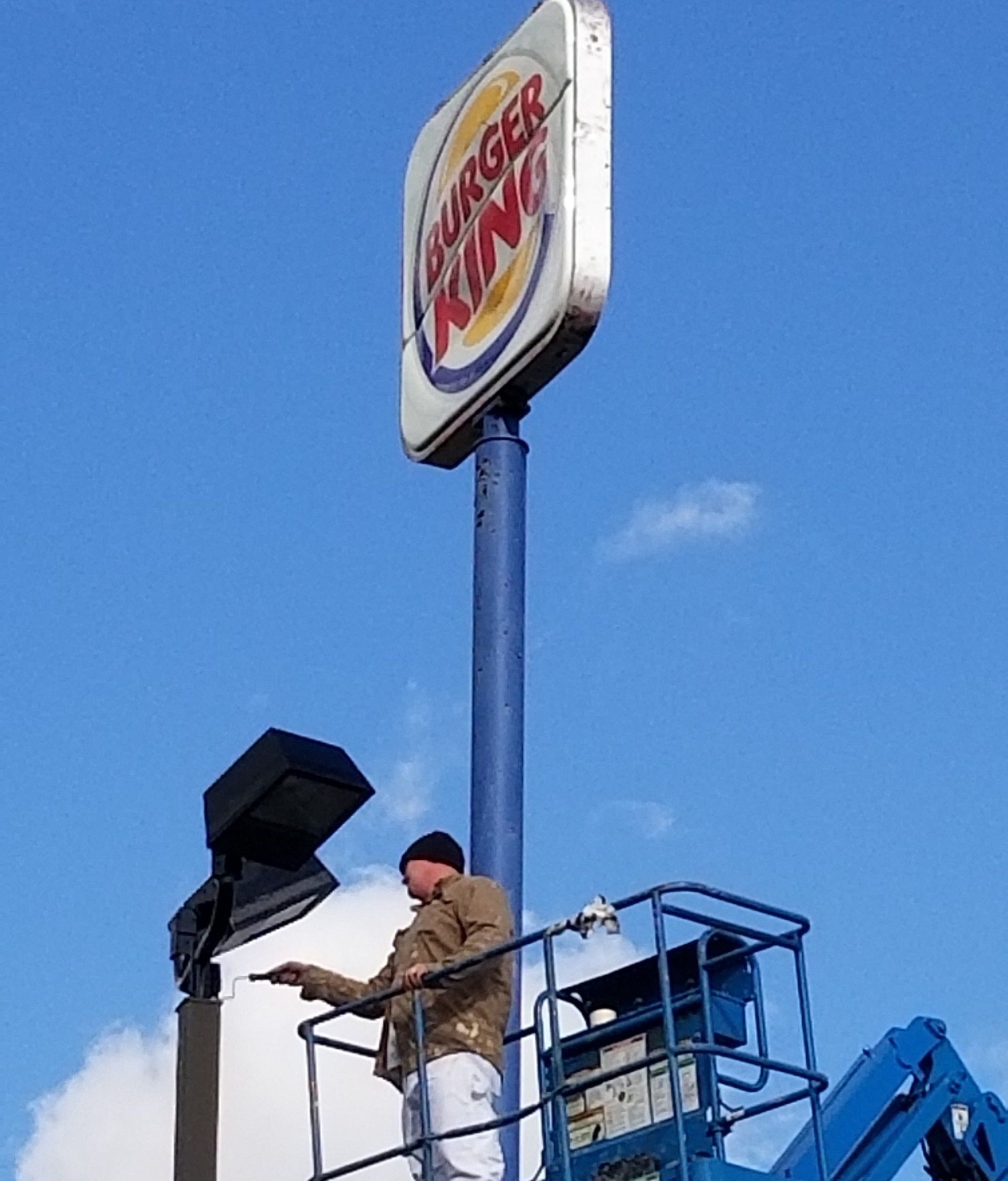 Worker on a lift replacing a Burger King sign against a blue sky