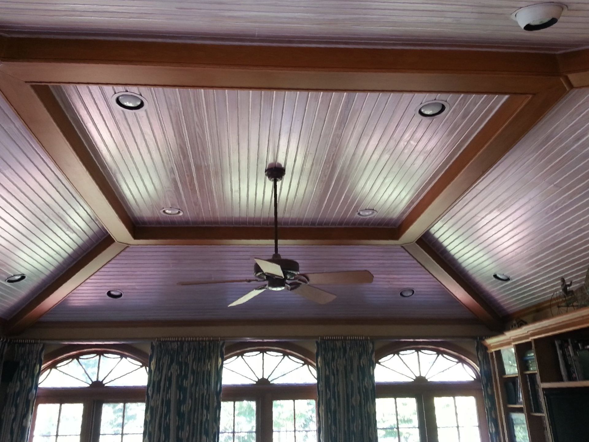 Wood-paneled coffered ceiling with recessed lights and a ceiling fan above arched windows