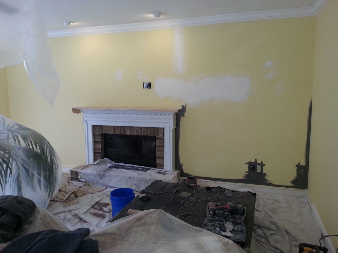 Living room under renovation with fireplace, patched yellow walls, and protective drop cloths on the floor