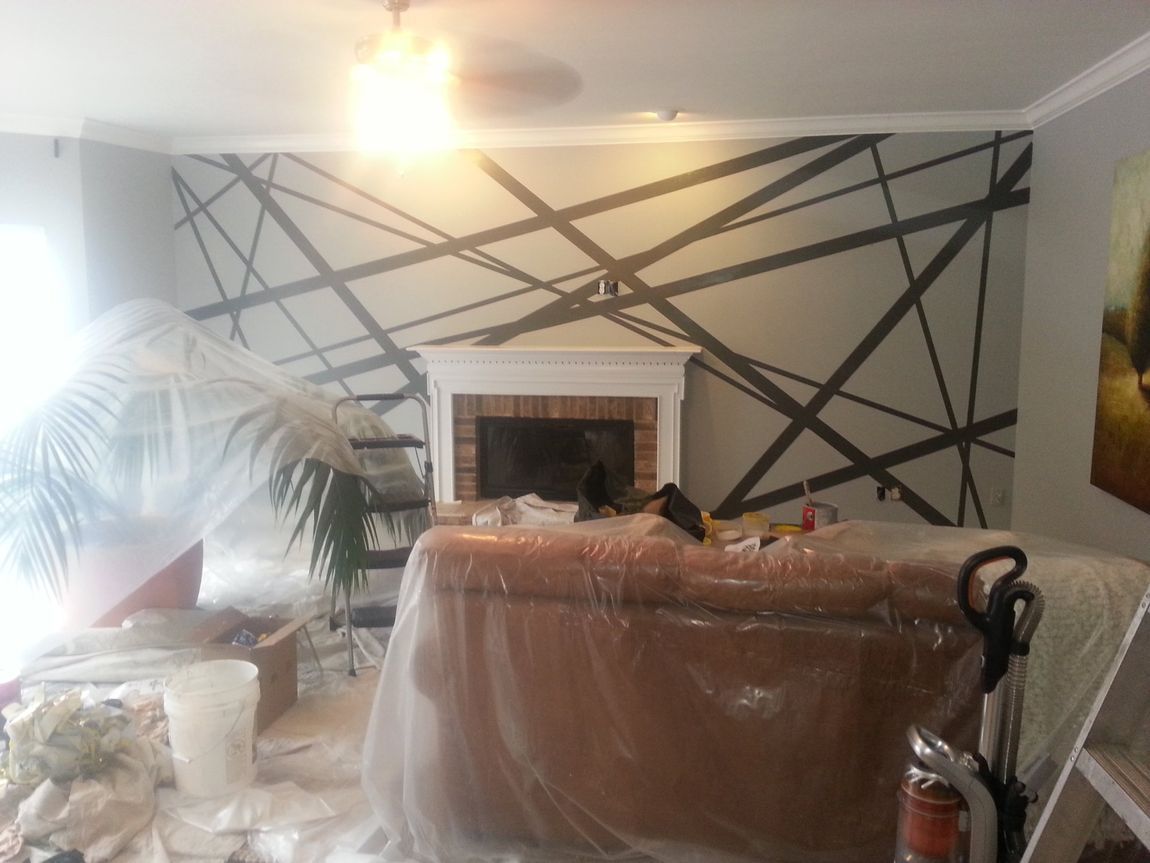Living room under renovation with taped-off wall lines and furniture covered in plastic wrap