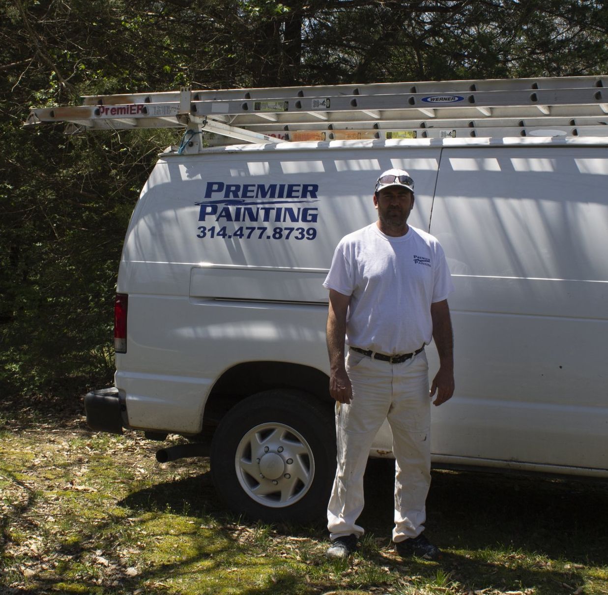 Painter standing beside a white Premier Painting van in a grassy yard