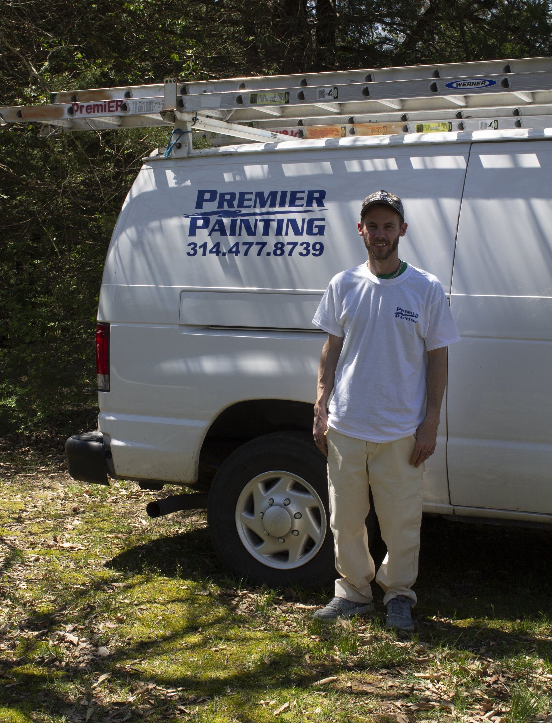 Man standing beside a white Premier Painting work van in a wooded area.