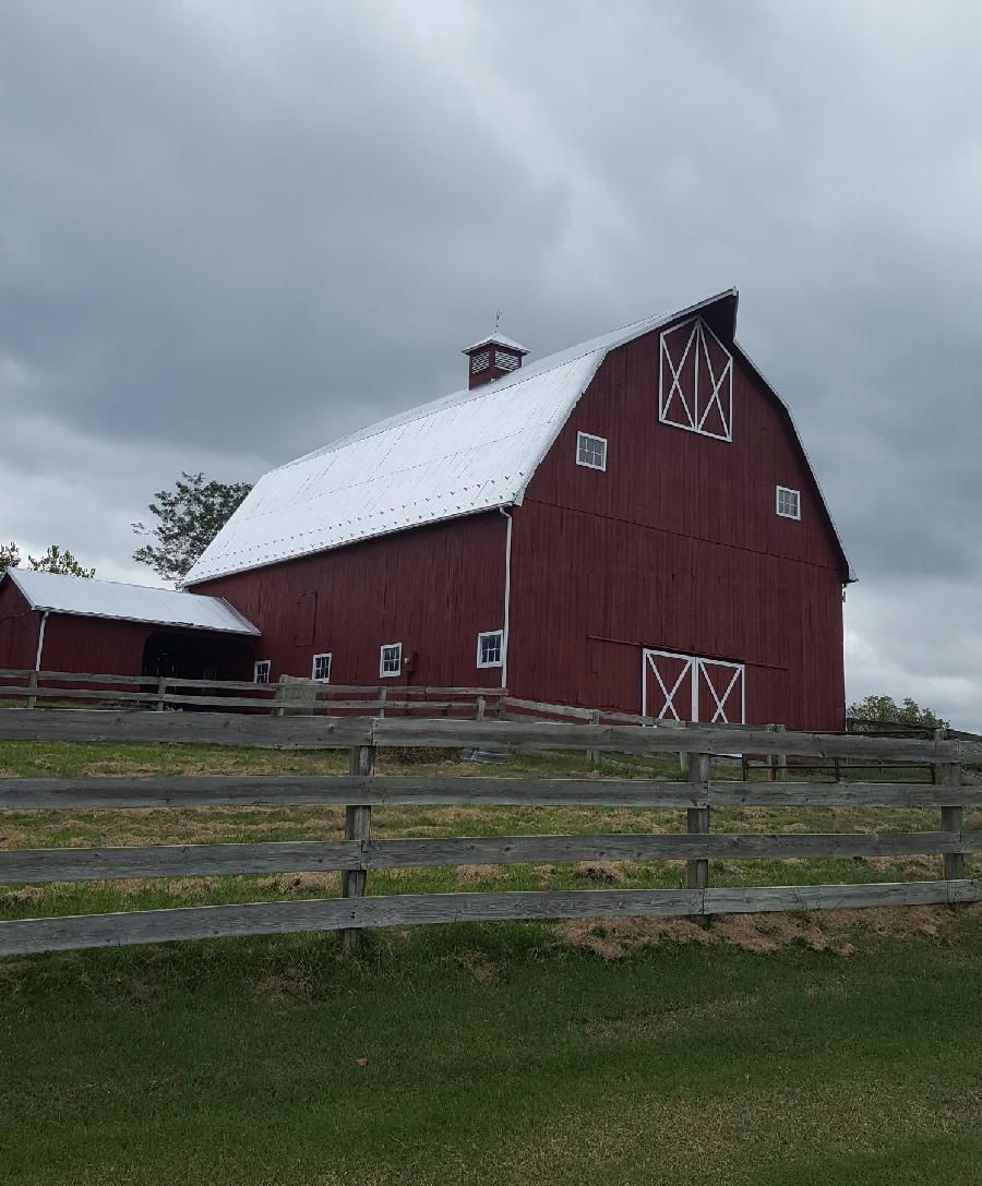 Red barn with a white roof behind a wooden fence under a cloudy sky