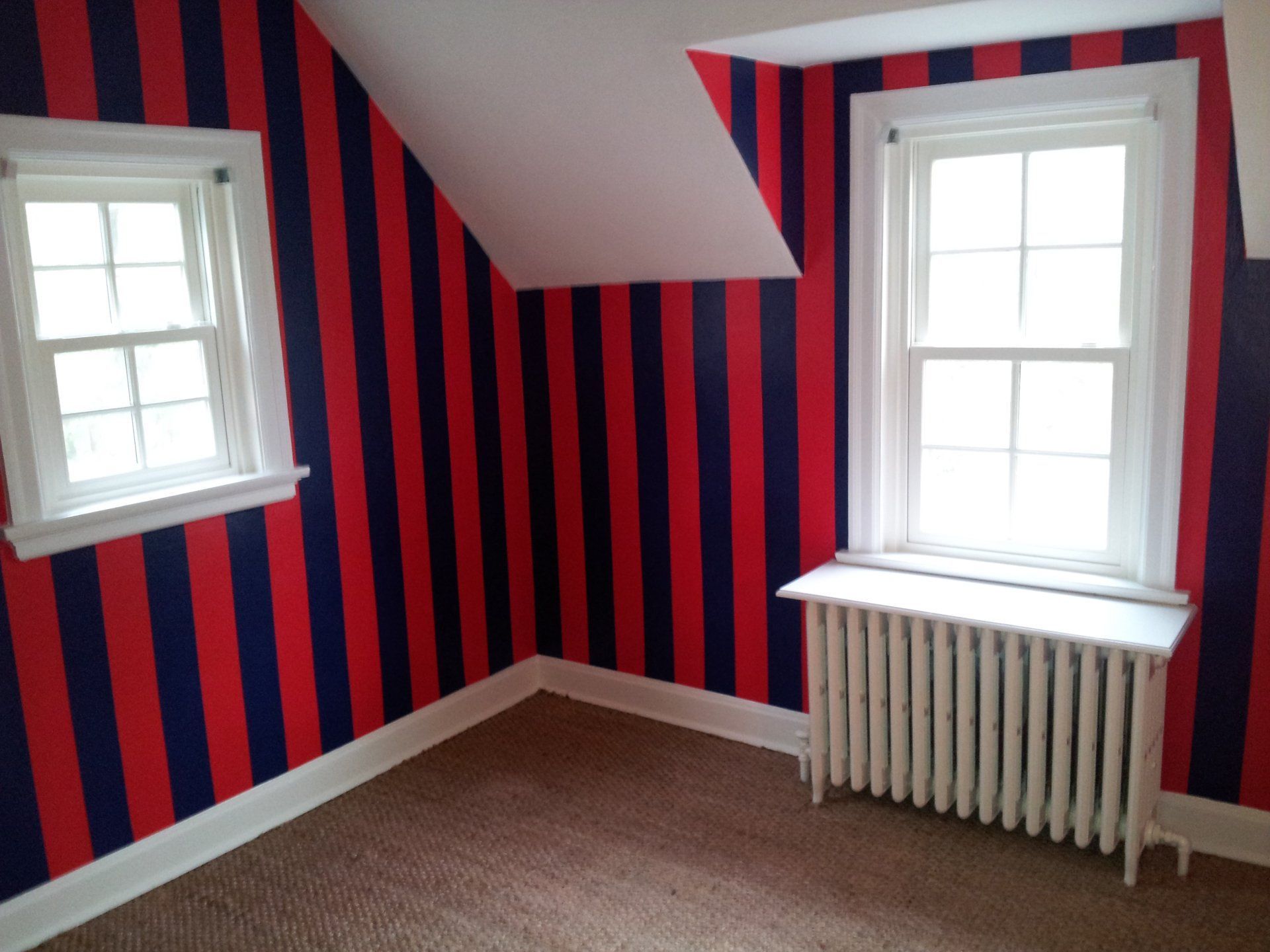 Small empty room with red-and-navy striped walls, two windows, and a radiator under one window.