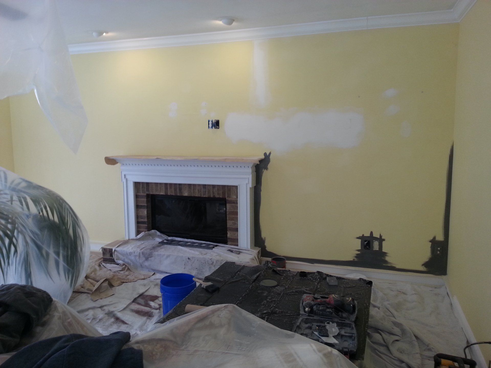 Living room under renovation with patched yellow walls, a fireplace, and drop cloths on the floor