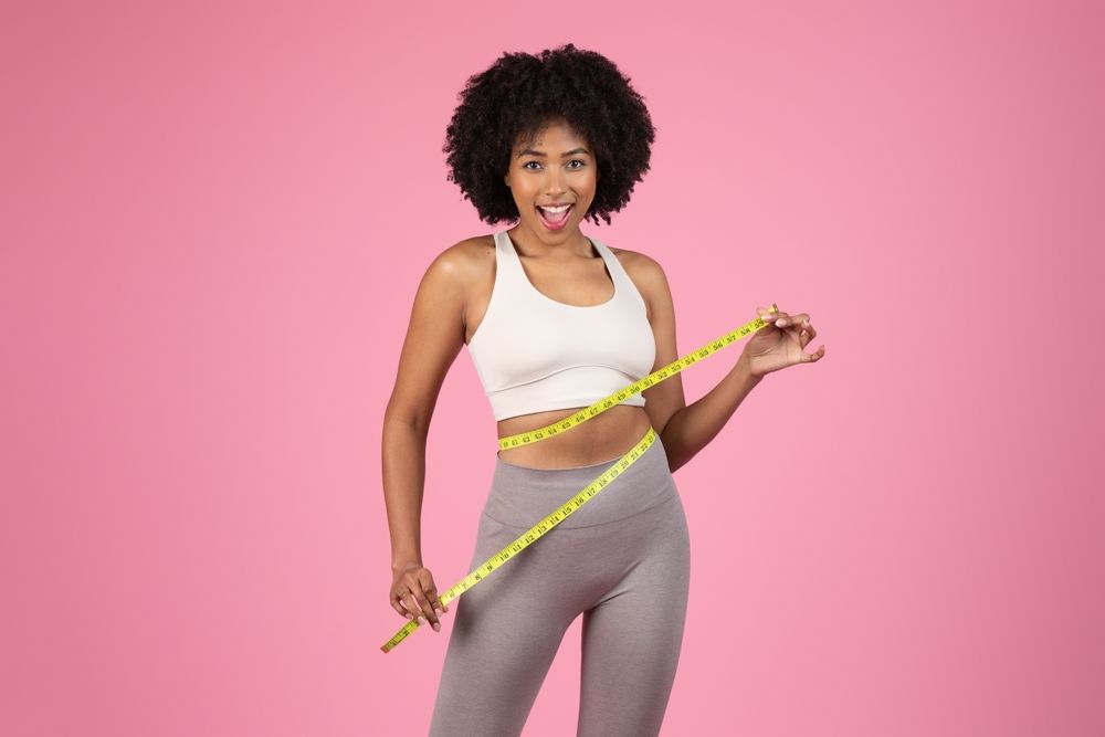 Woman measuring her waist with a yellow tape against a pink background