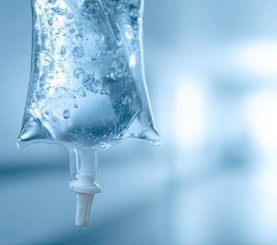 Clear IV drip bag hanging with a white tube against a soft blue background