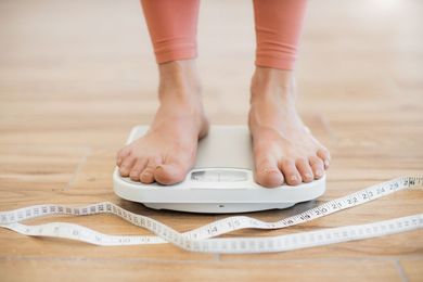 Feet on a bathroom scale beside a measuring tape on a wooden floor