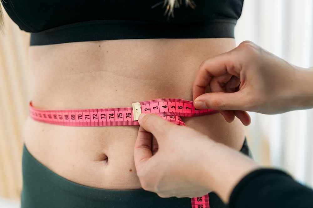 Hands measuring a waist with a pink tape measure