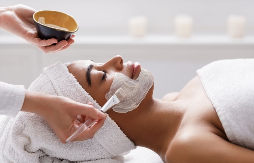Spa facial treatment with cream being applied to a woman lying on a bed with a towel headband