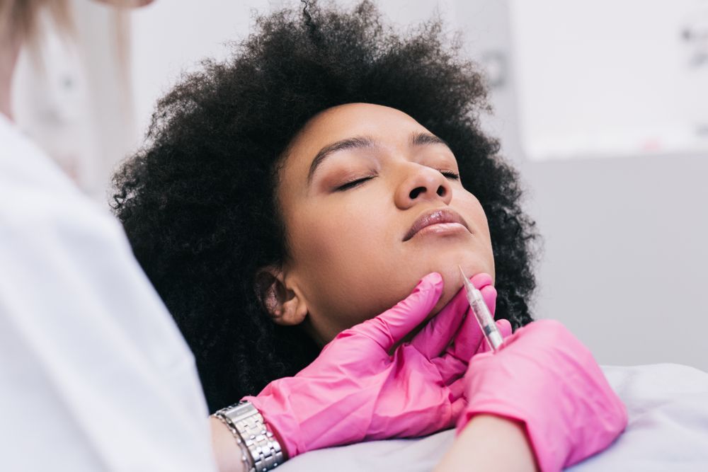 Person receiving facial treatment while a practitioner wearing pink gloves massages the chin and neck